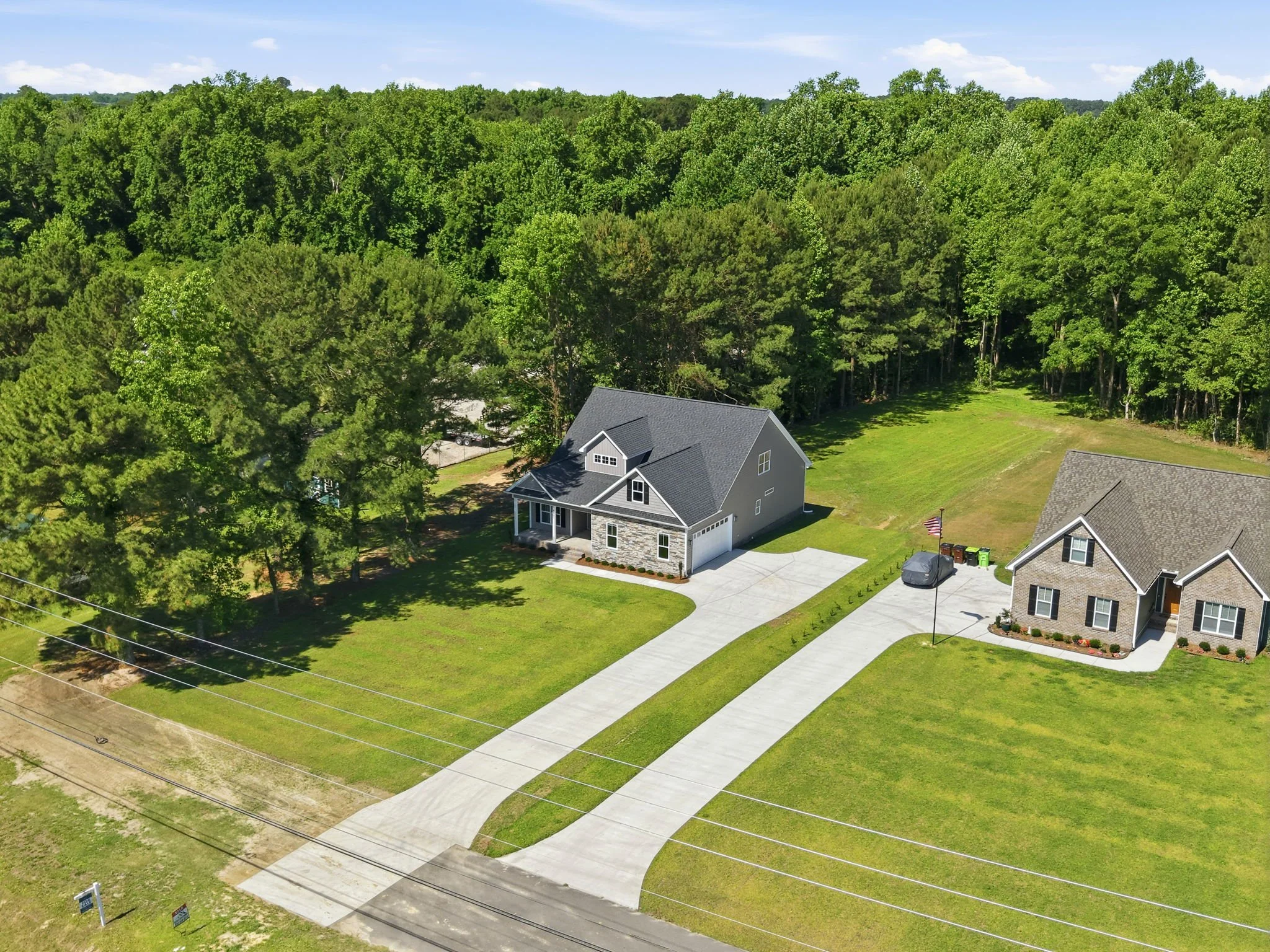 Aerial view of a house with a drive and lawn, surrounded by a forest of tall green trees on a sunny day.