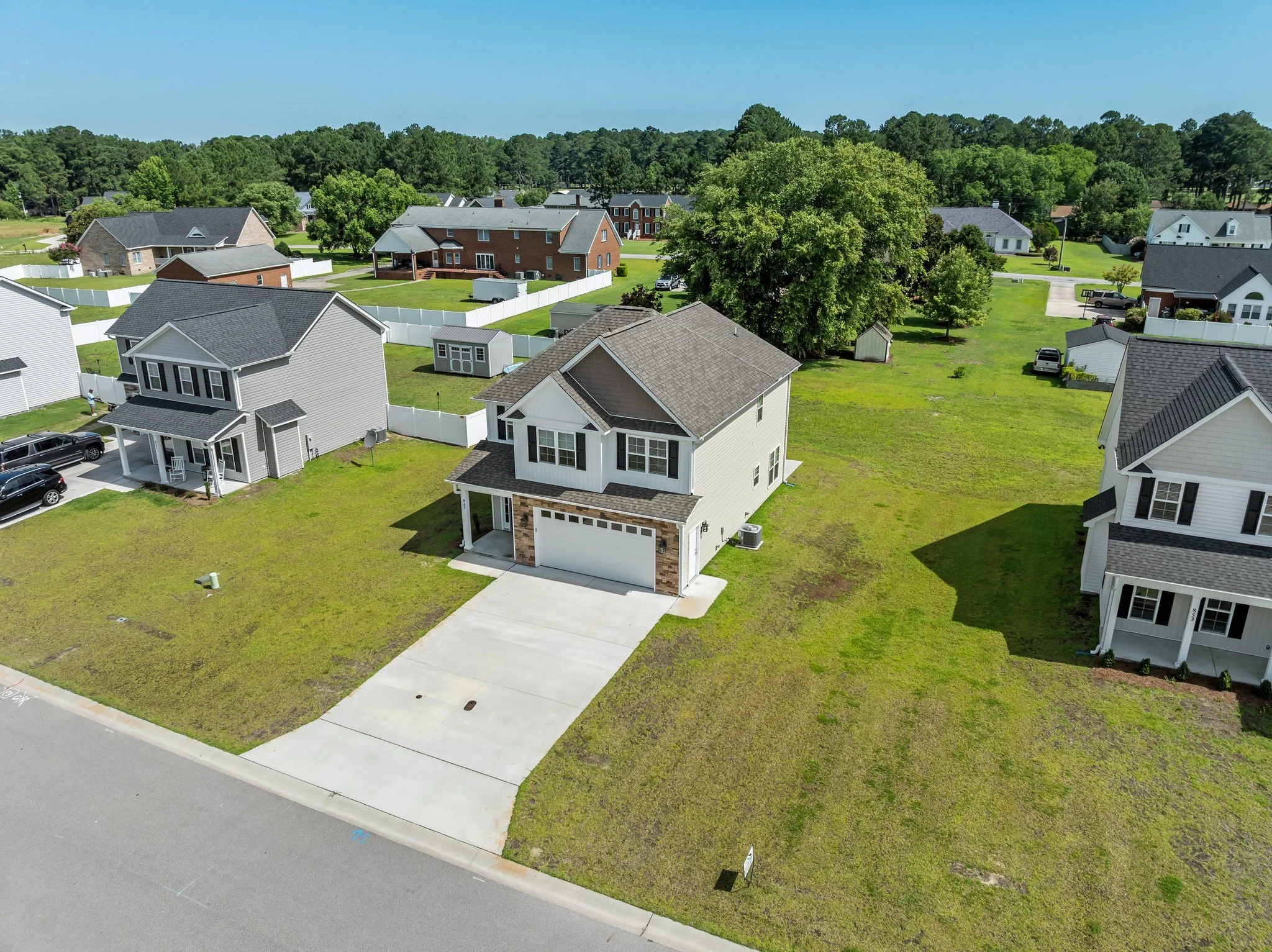 Aerial view of a suburban neighborhood with houses, green lawns, and trees under a clear blue sky.