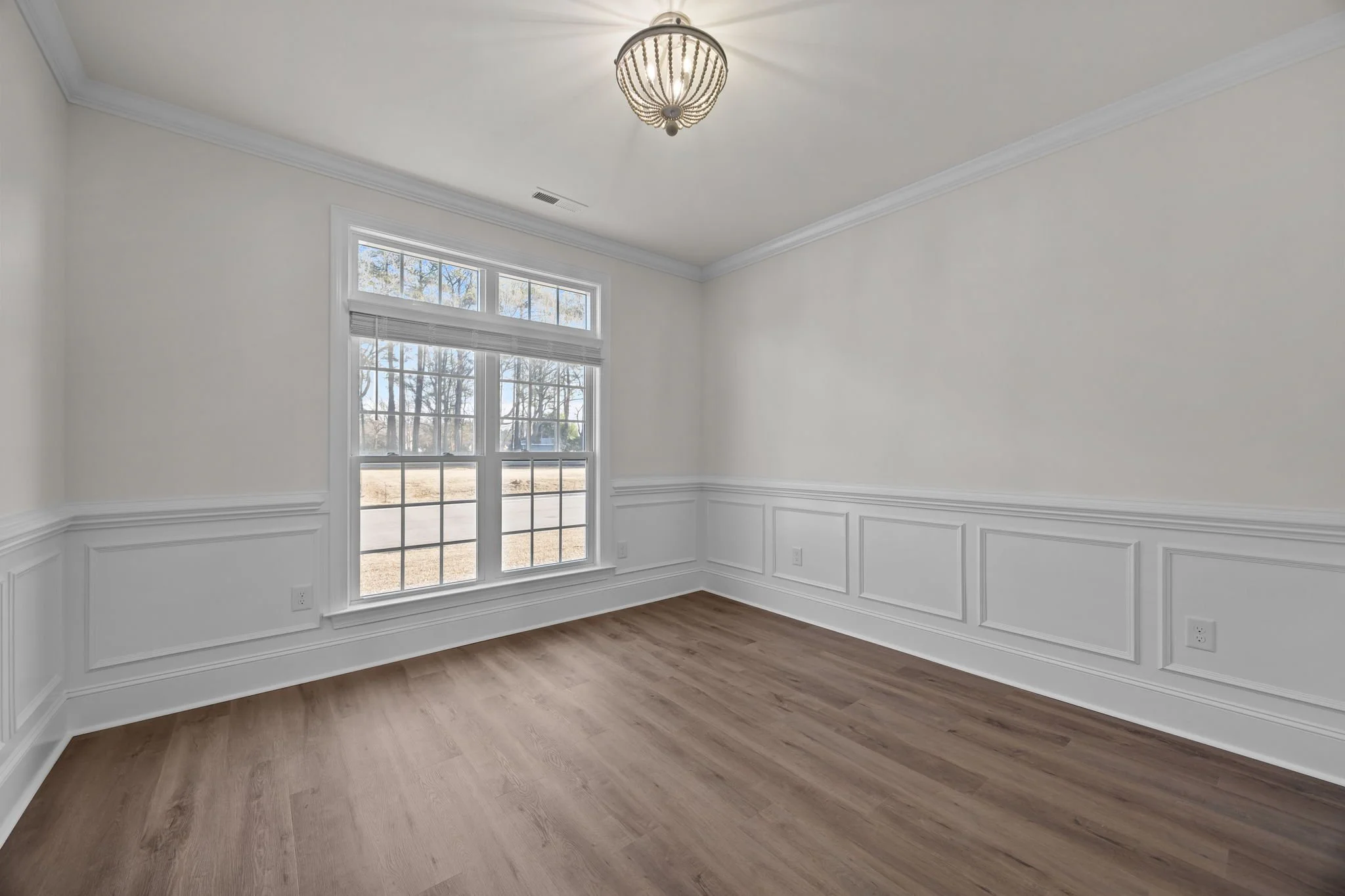 Empty room with large window, white walls, wood flooring, crown molding, and a ceiling light fixture.