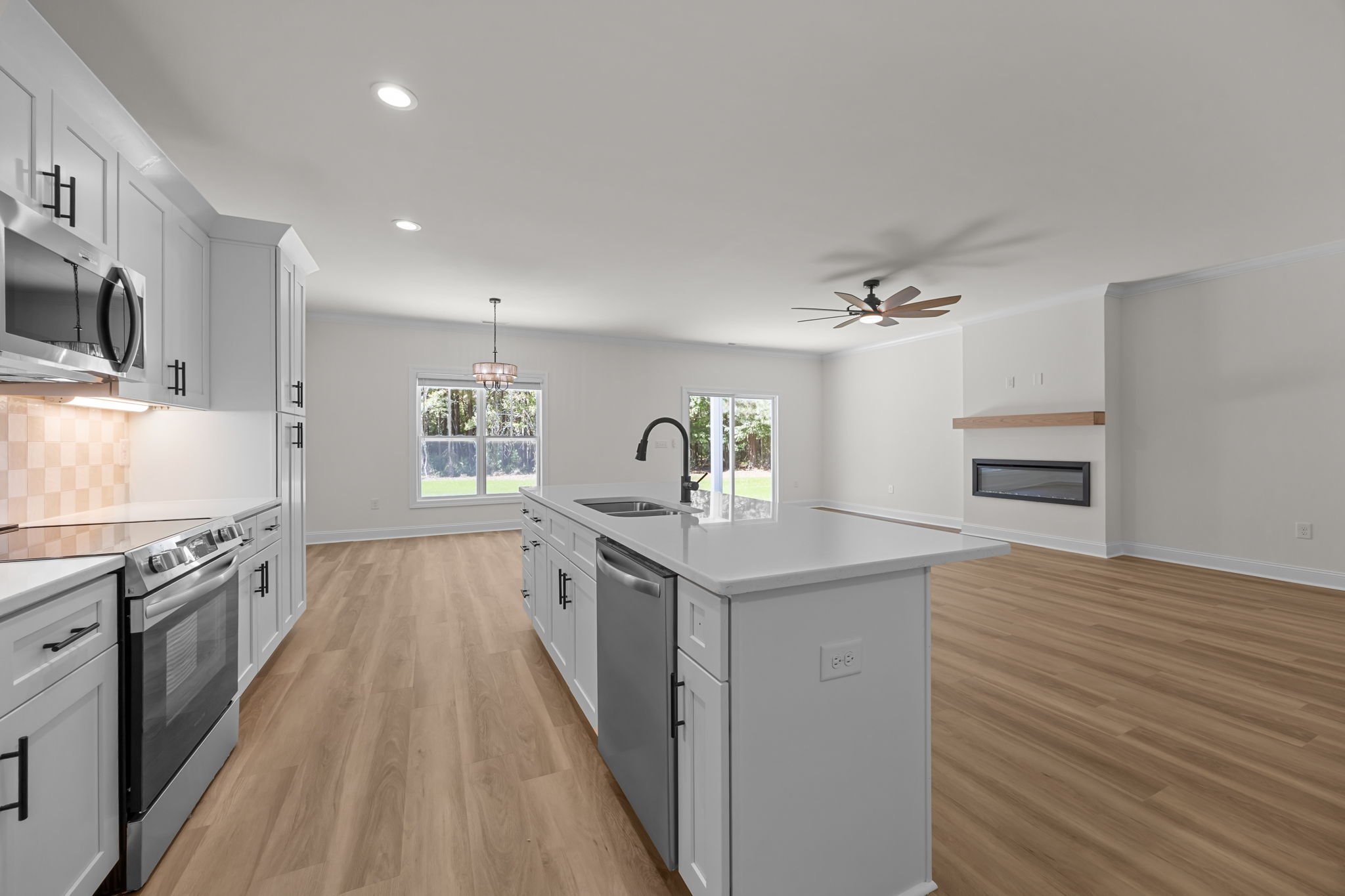 Modern kitchen with white cabinets, stainless steel appliances, an island with a sink, hardwood floors, and large windows.