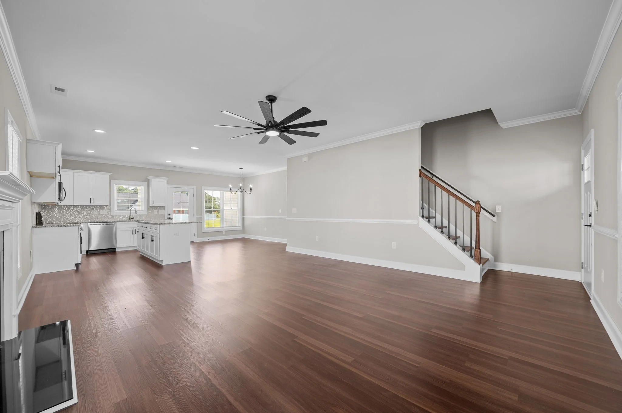 Open-concept living room and kitchen area with hardwood floors, white cabinetry, a ceiling fan, and large windows in a modern home.