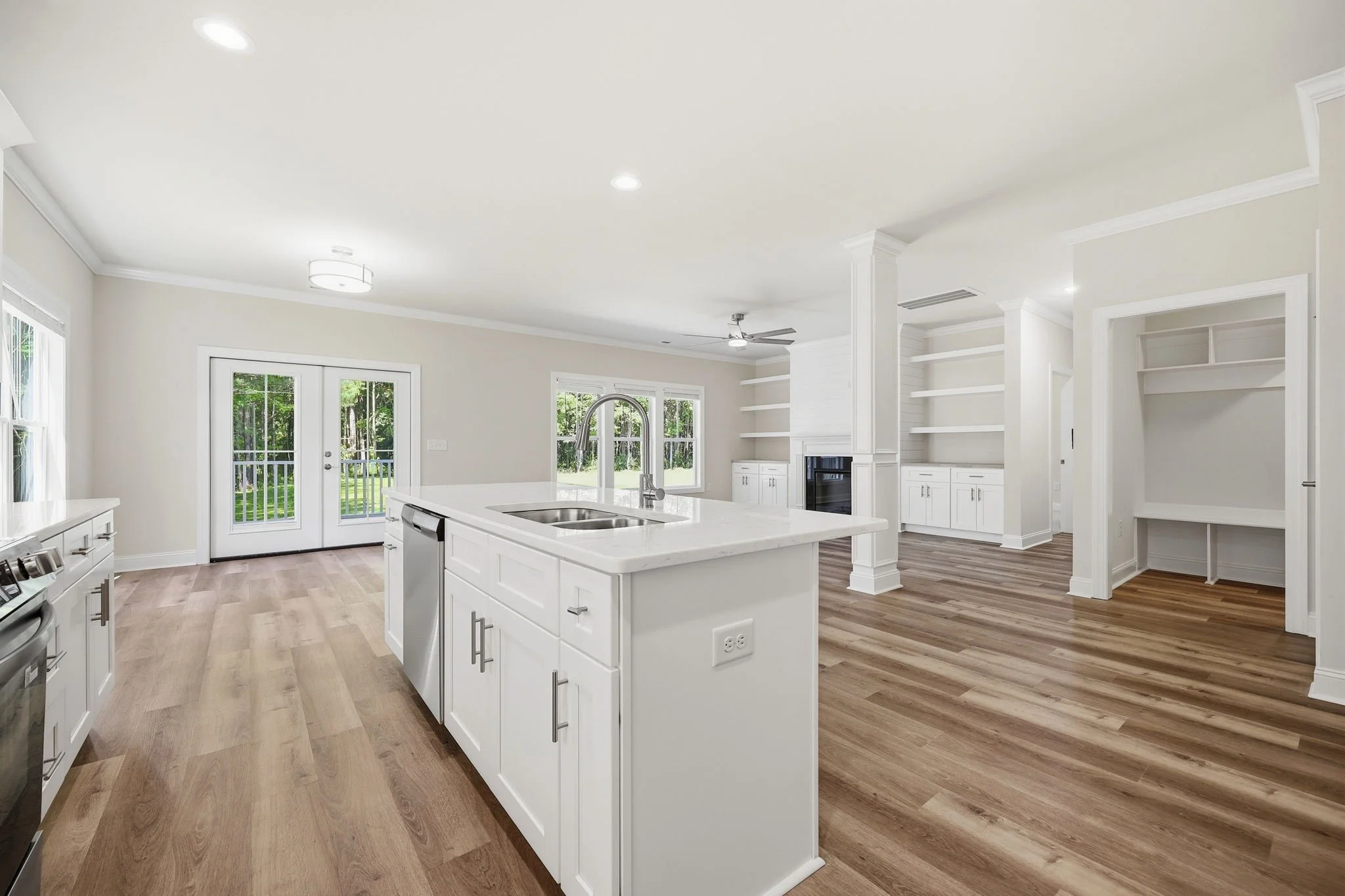 Bright modern kitchen with white cabinetry, a kitchen island with a double sink, large windows, and wooden flooring.