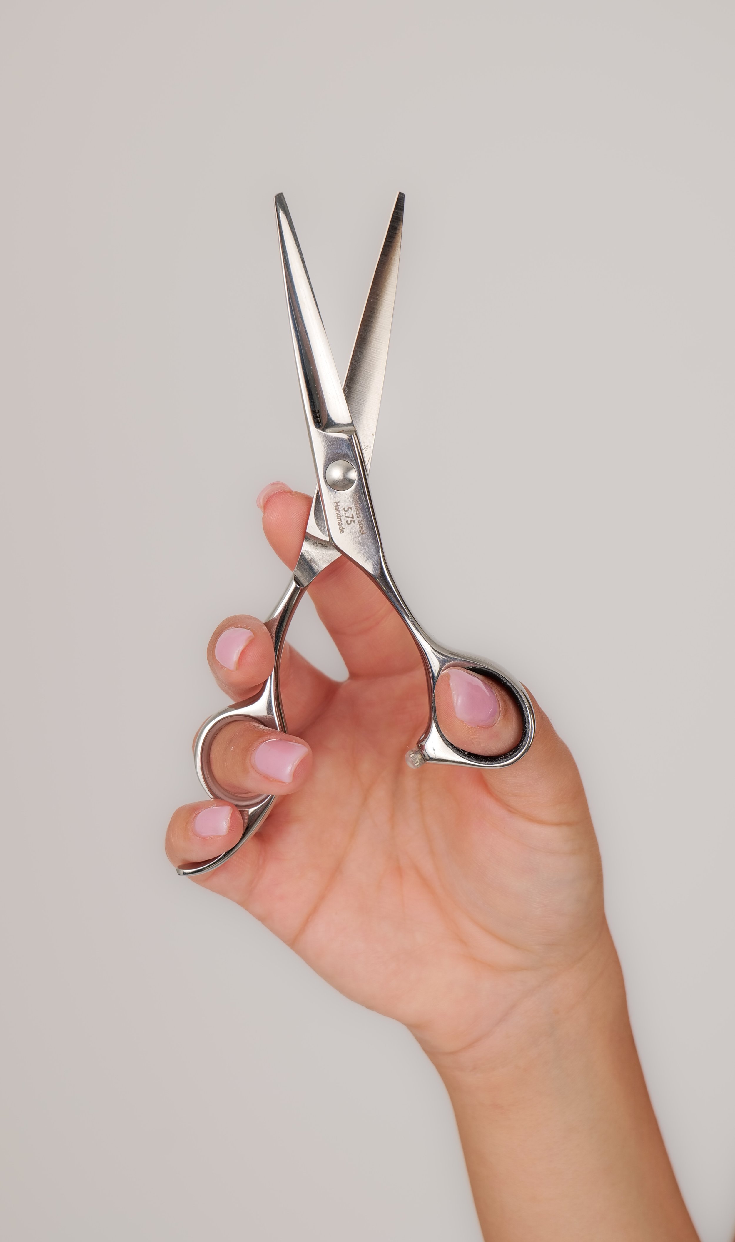 A hand holding a pair of small, shiny stainless steel scissors against a plain light background.