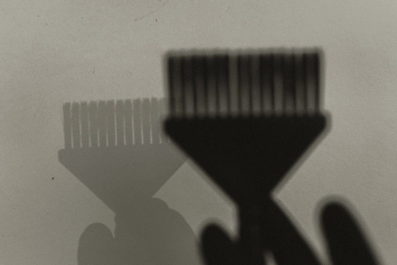 Shadow of a hand holding a small comb on a flat surface.