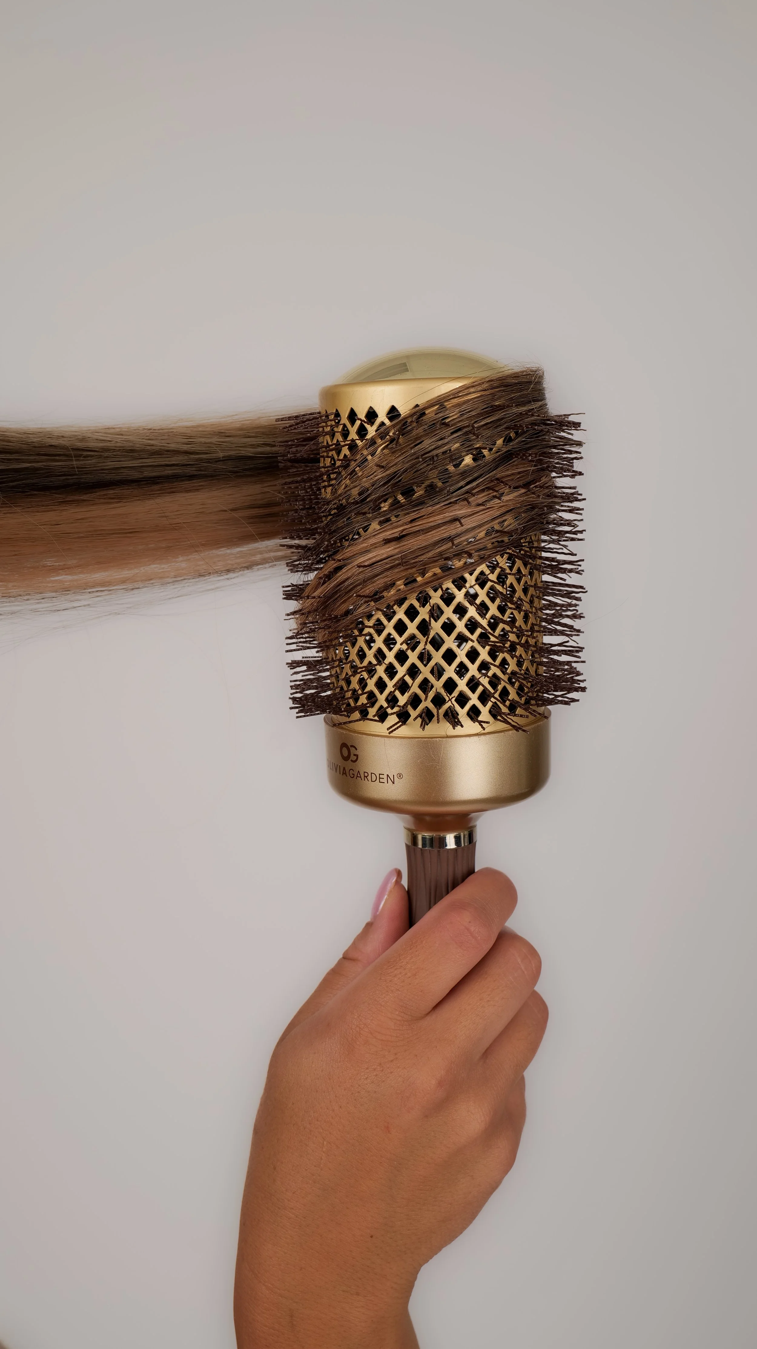 Person holding a round hairbrush with brown bristles and a metallic gold handle.