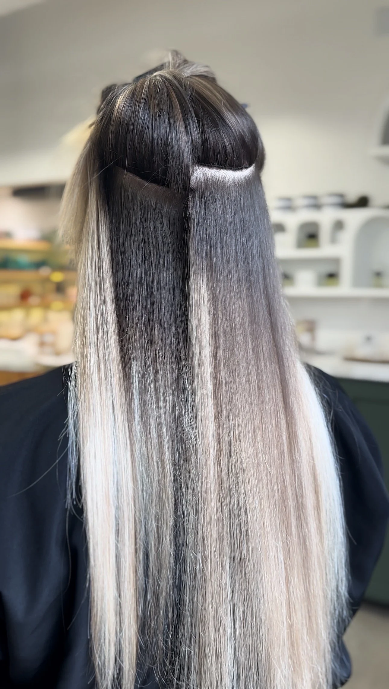 Back view of a person with partially cut and texturized hair, colored in shades of black, gray, and platinum blonde, in a salon setting.
