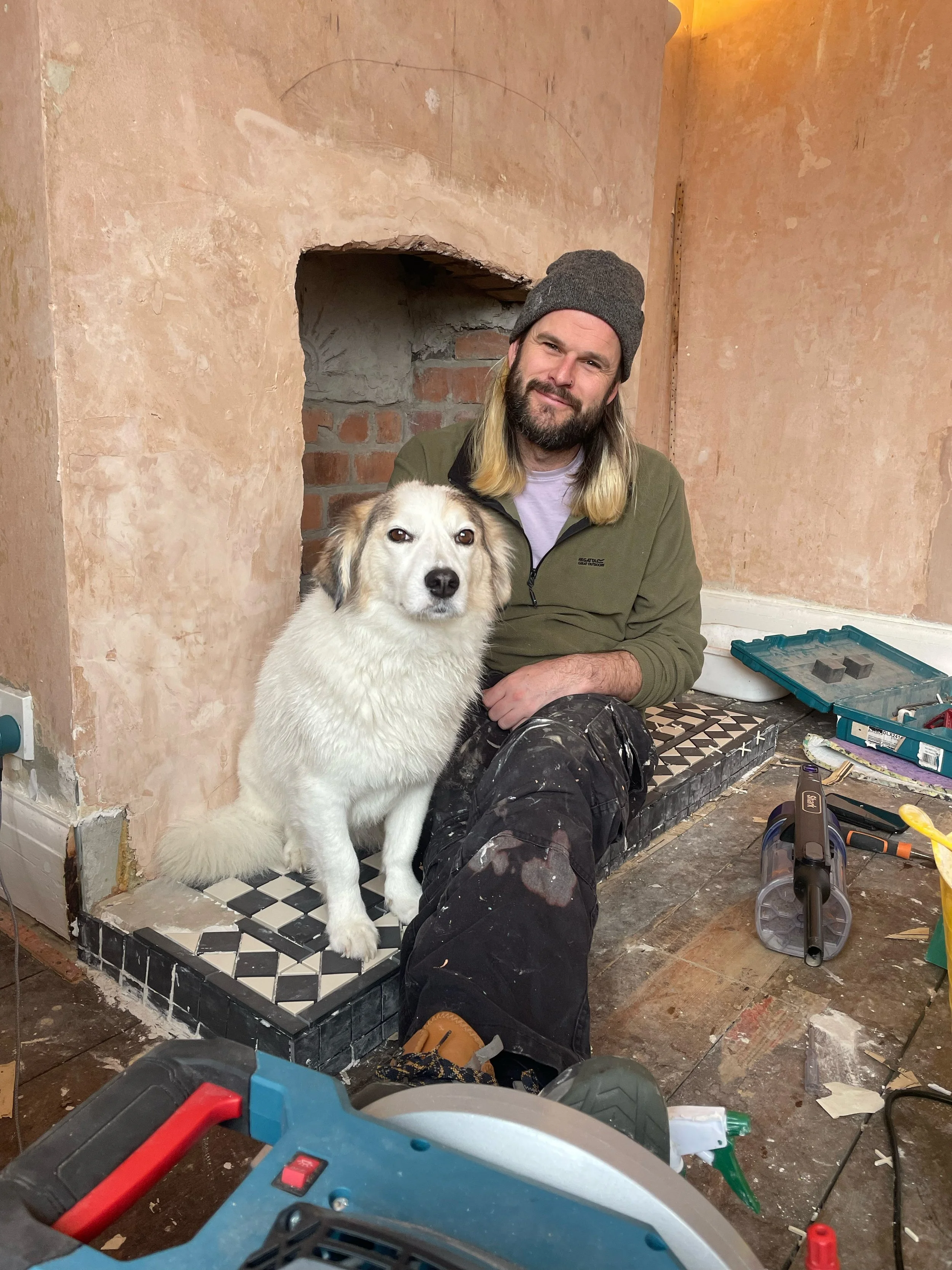 Bristol tradesman Finn Magee sitting with his dog by a restored period fireplace hearth.