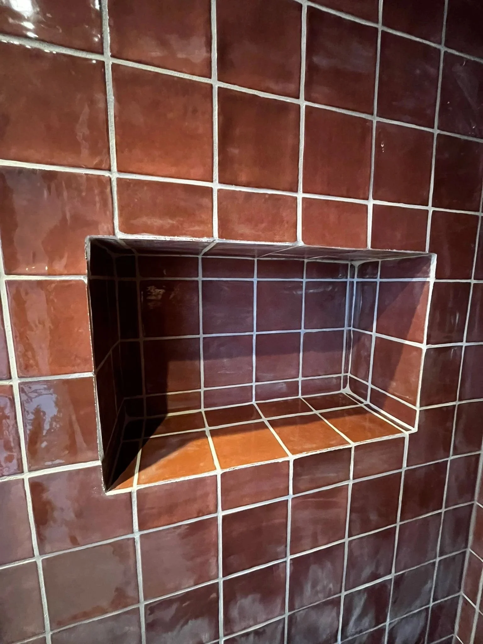 Close-up of a tiled wall with a built-in niche or shelf, covered with brown ceramic tiles with white grout lines.