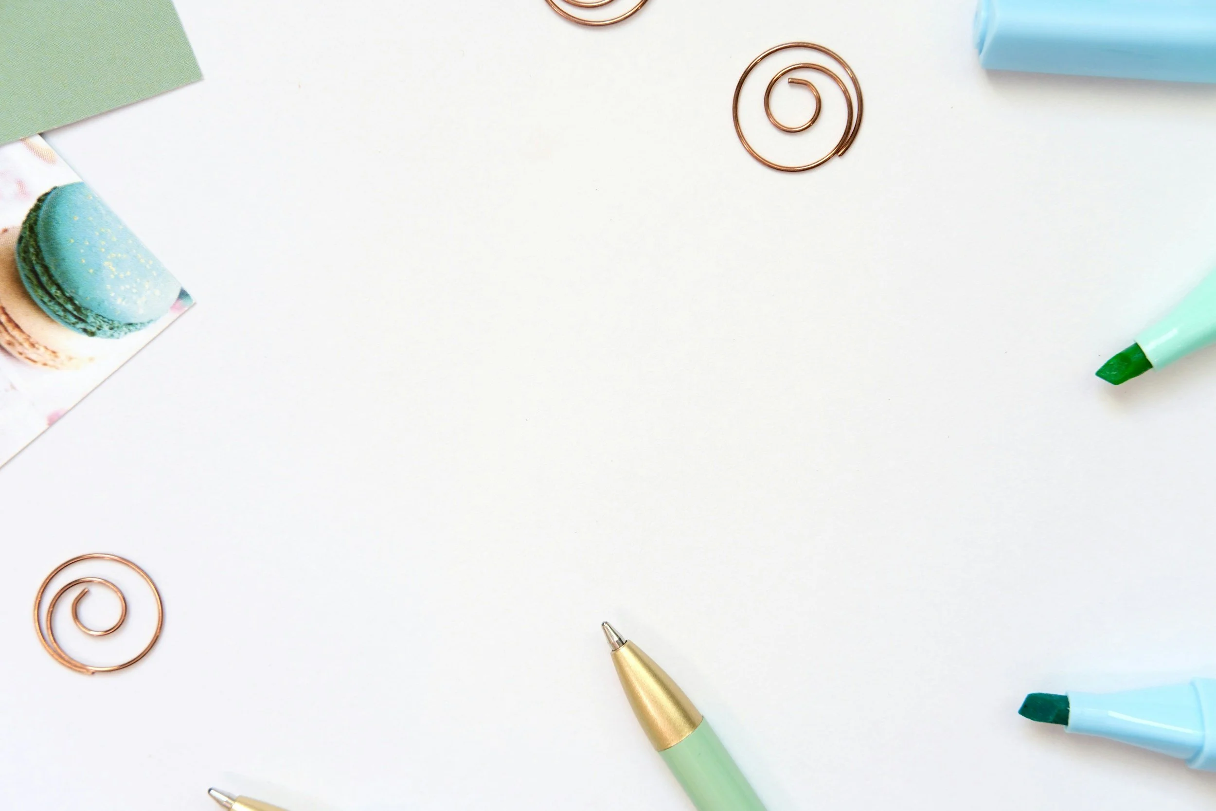 A background of colourful office and craft supplies on a white background, including paper clips, a green marker, a gold pen, and decorative paper.