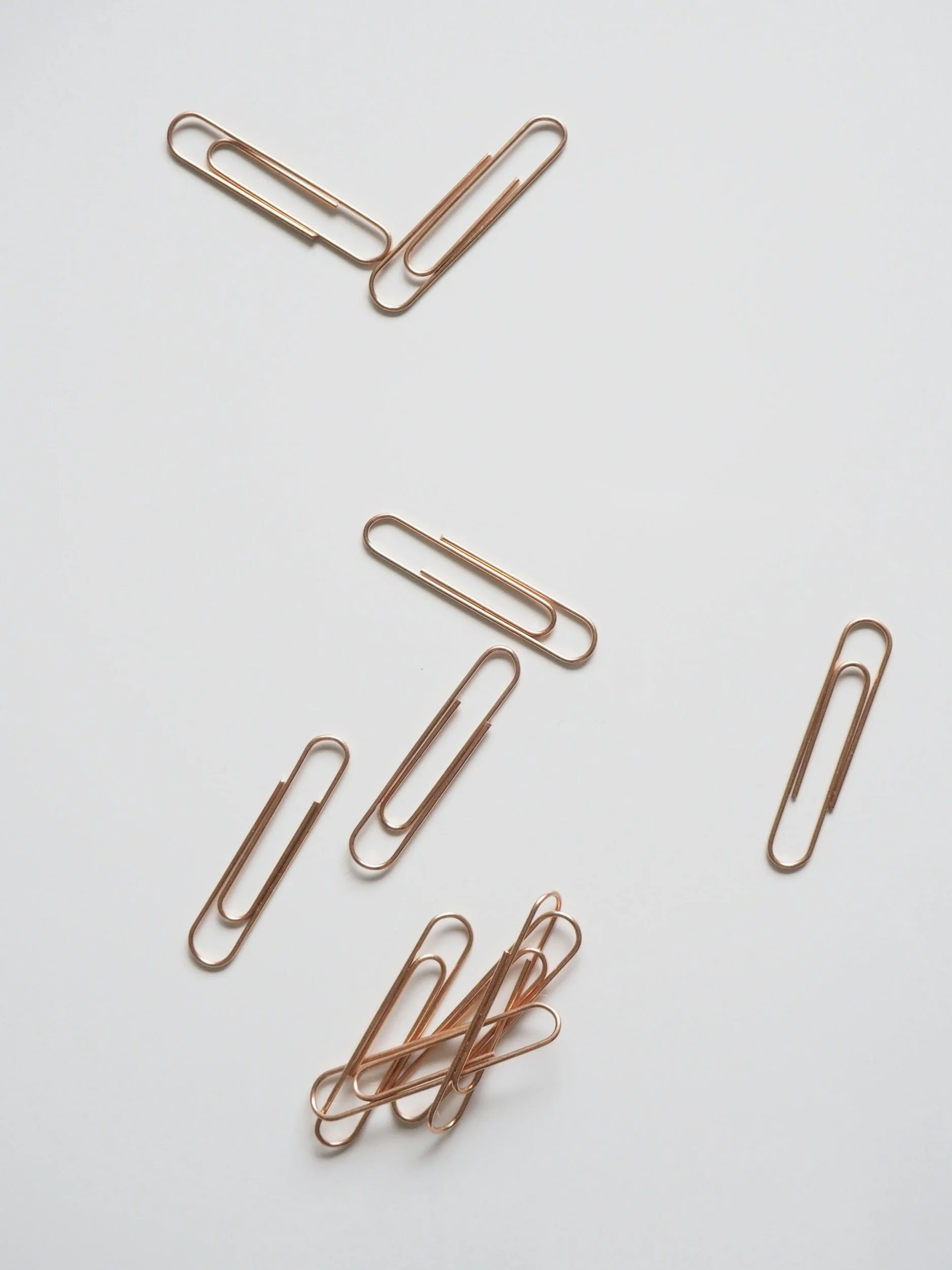 Several rose gold paper clips scattered on a white surface.