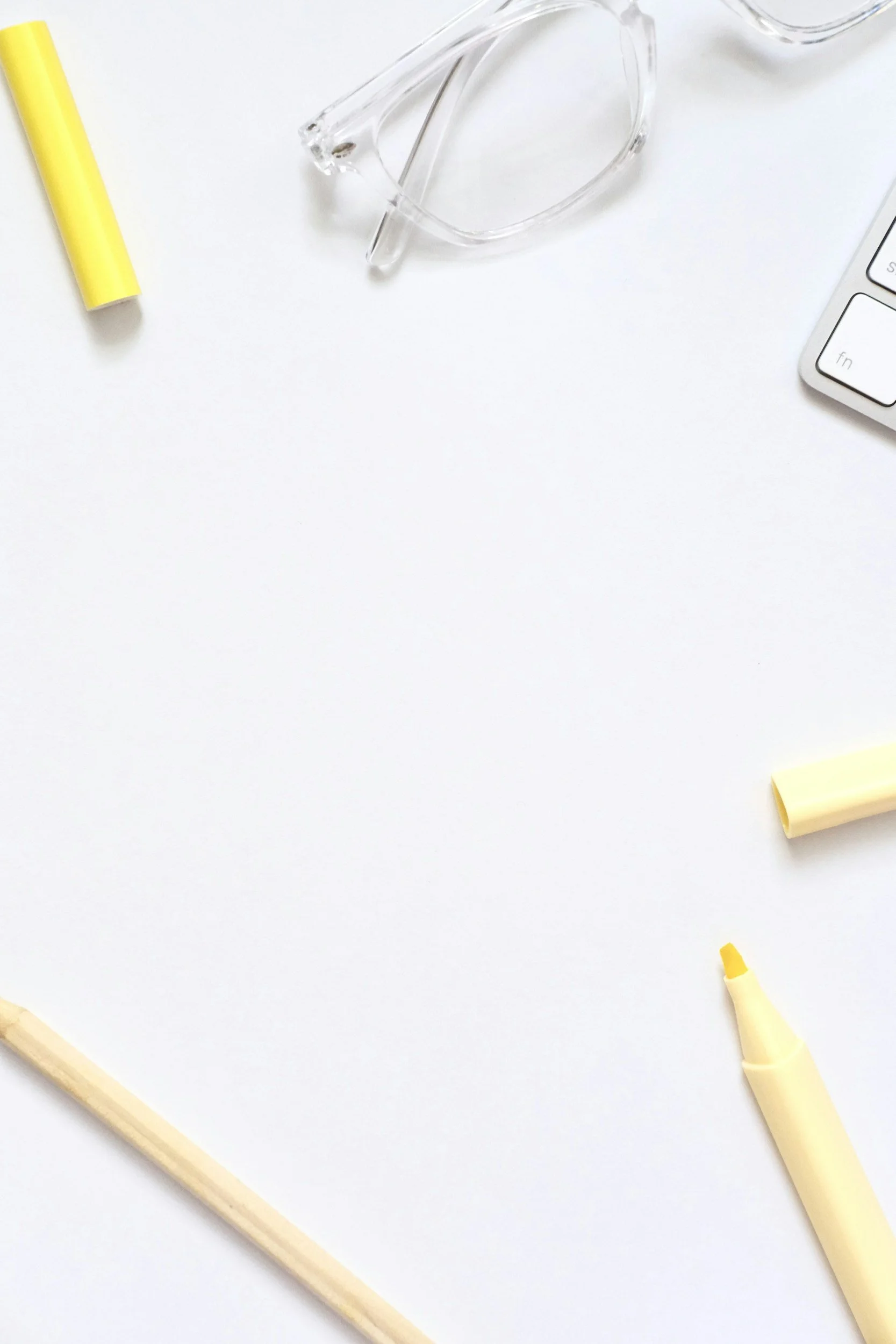 A background Close-up of a white sheet of paper with yellow markers, a clear pair of glasses, and a part of a white keyboard.