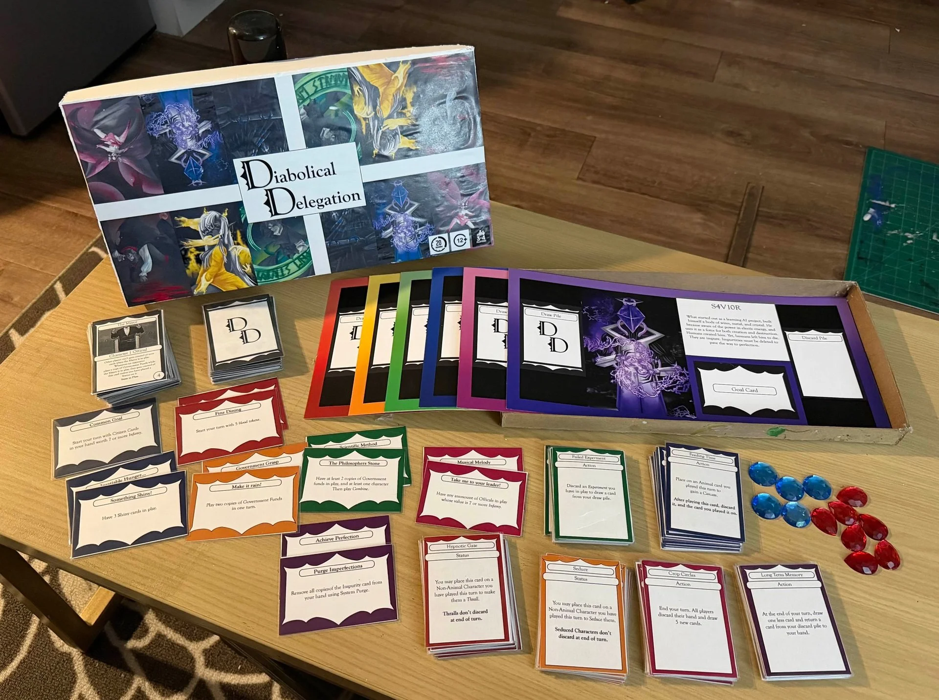 A tabletop game setup called 'Diabolical Delegation,' featuring colorful cards with instructions, some stacks of cards, game tokens, and a game box with artwork depicting fantasy characters and mythical creatures.