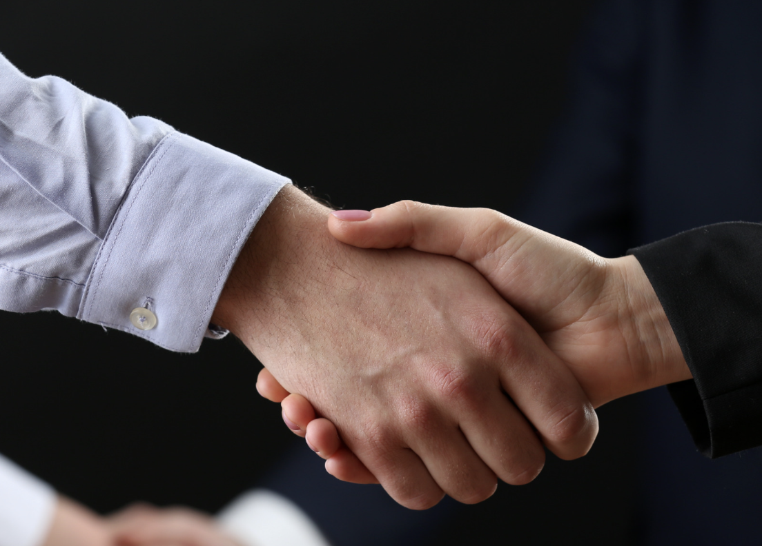 Two people shaking hands, one in a white shirt and the other in a black suit.