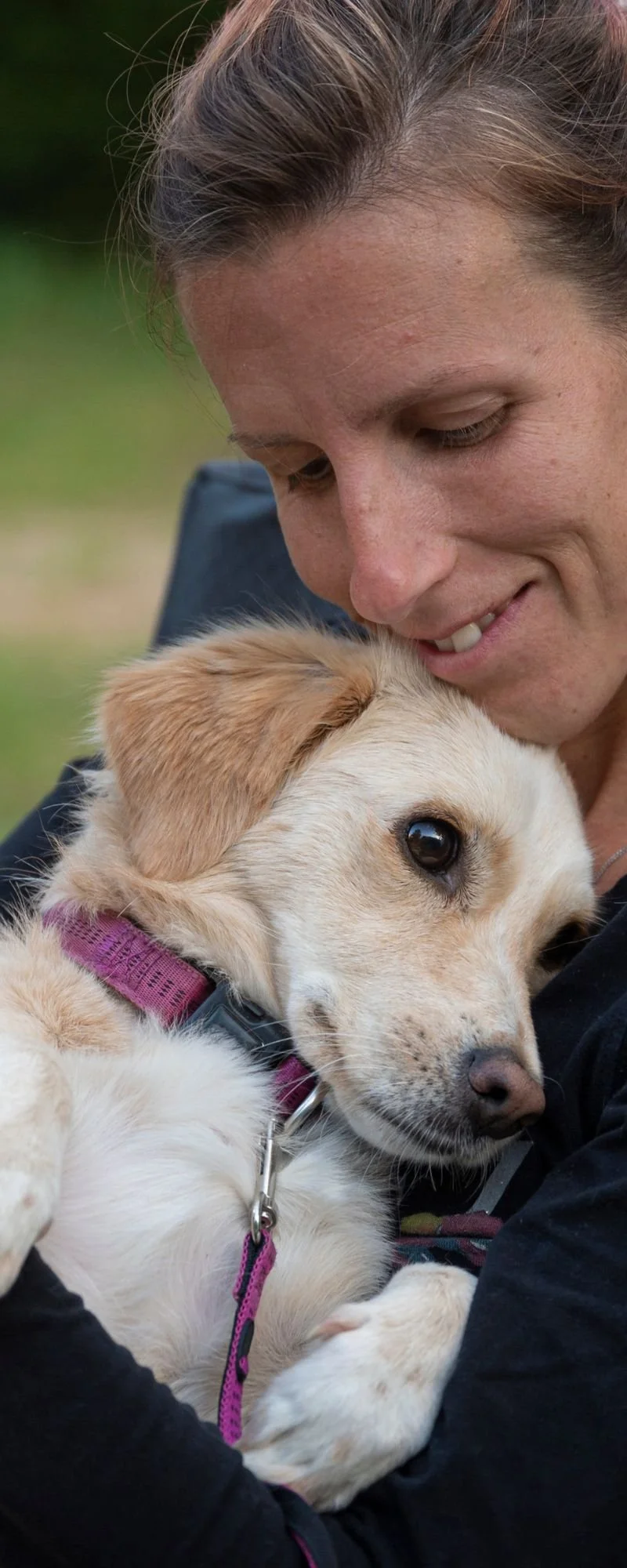 A woman hugging a cute puppy outdoors, with a blurred green background.