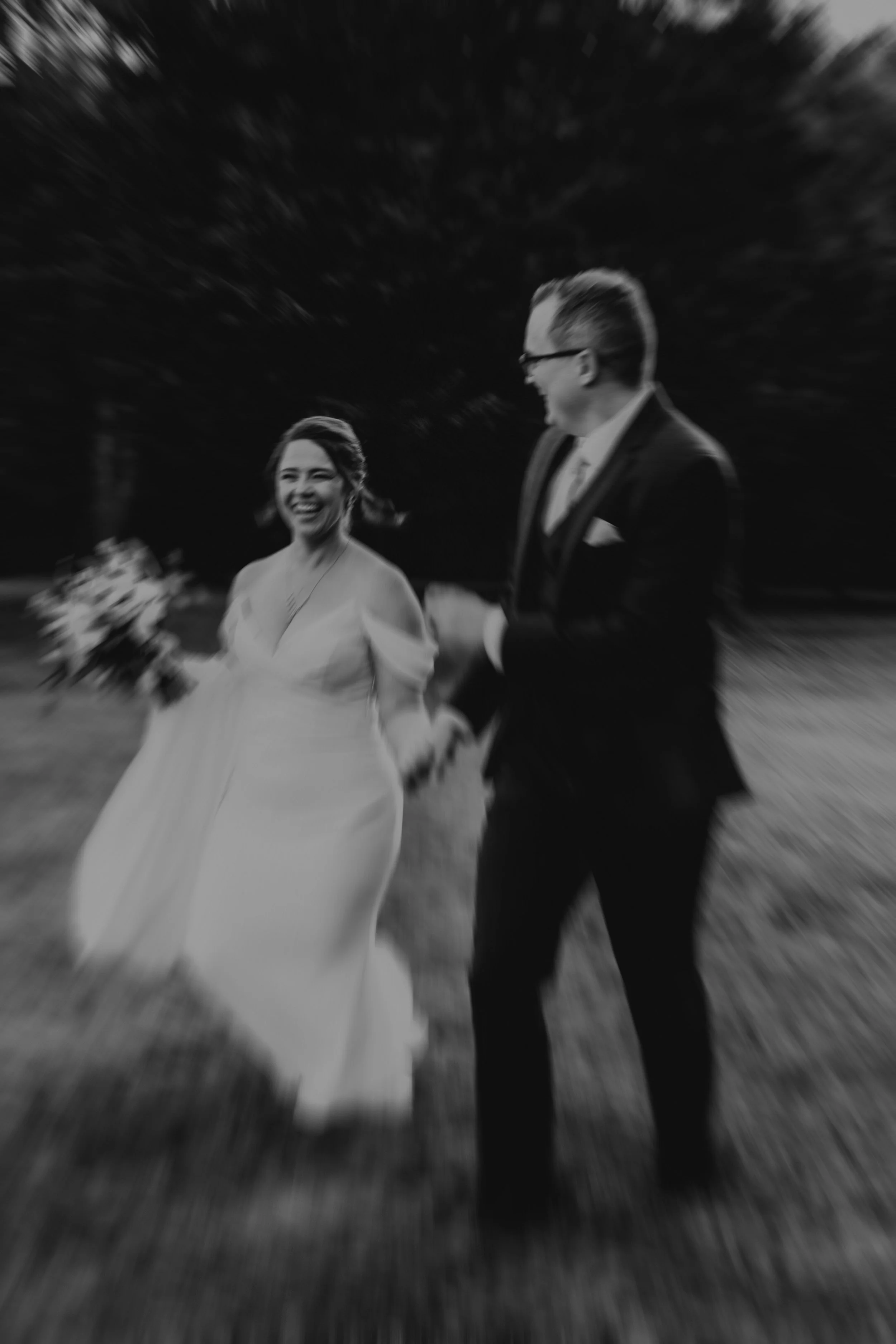 A bride and groom walking outdoors at night, smiling and holding hands, with a blurred background and motion effects.
