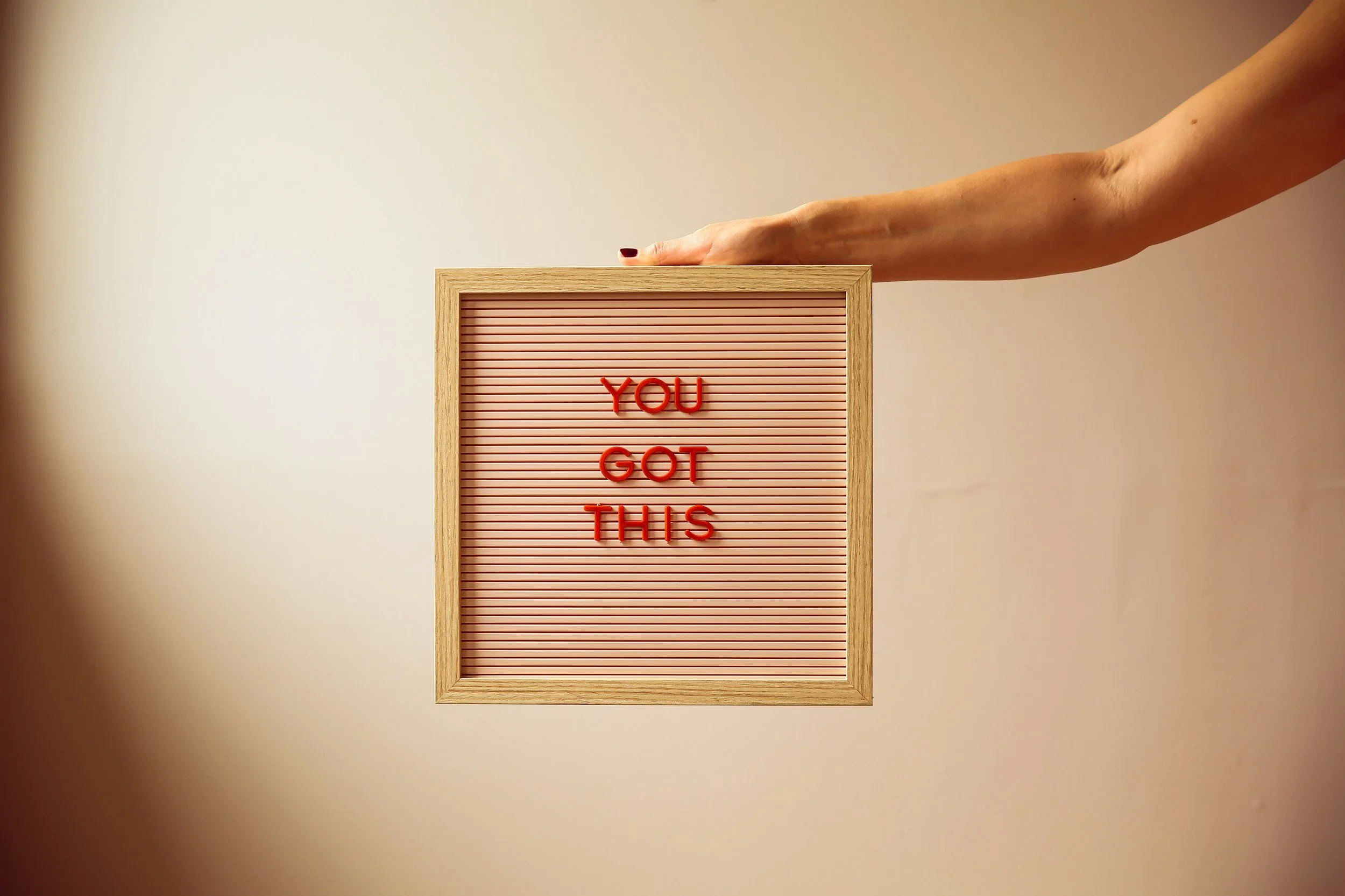 Hand reaching out to a letter board with the phrase 'YOU GOT THIS' written in red letters.