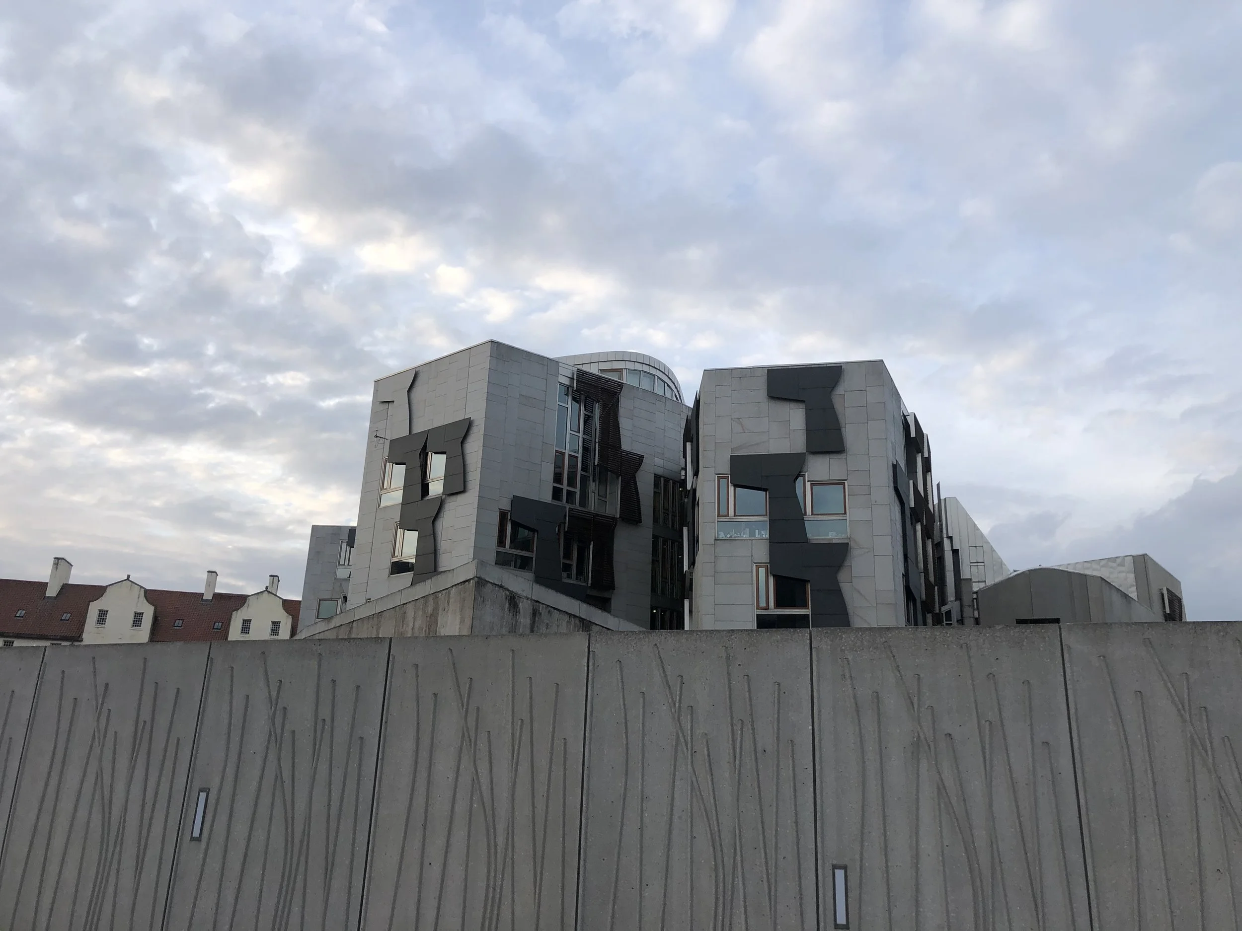 A modern multi-story building with an unusual architectural design featuring irregularly shaped windows and dark contrasting panels. The building is set against a cloudy sky with a mix of light and dark clouds.