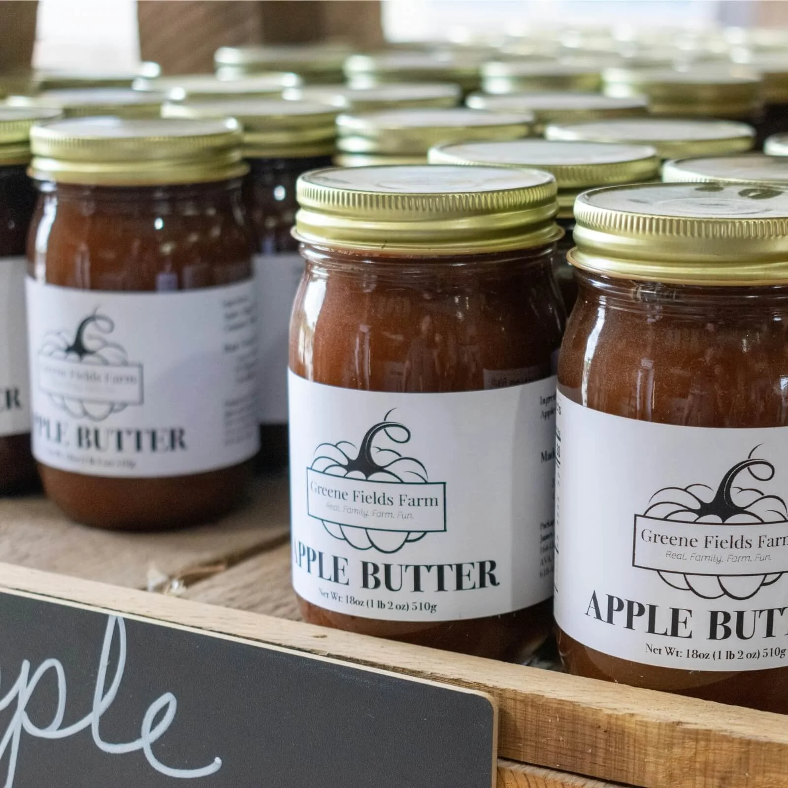 Jars of apple butter with white labels and gold lids on a wooden shelf at Greene Fields Farm.