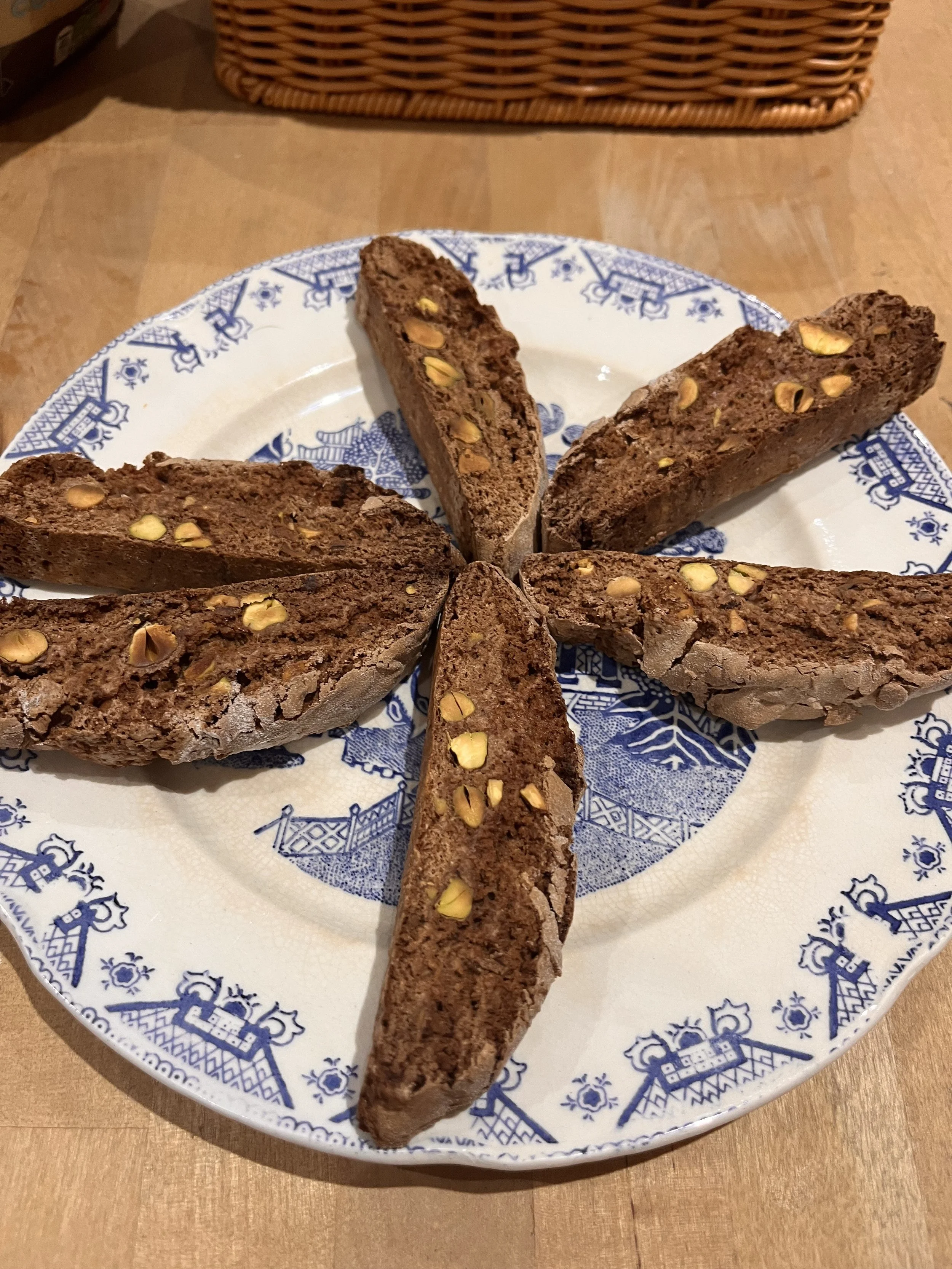 Slices of chocolate biscotti with chopped pistach nuts on a blue and white patterned plate.