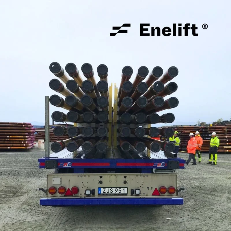 A flatbed truck carrying large pipes at a construction site with workers in safety gear in the background.