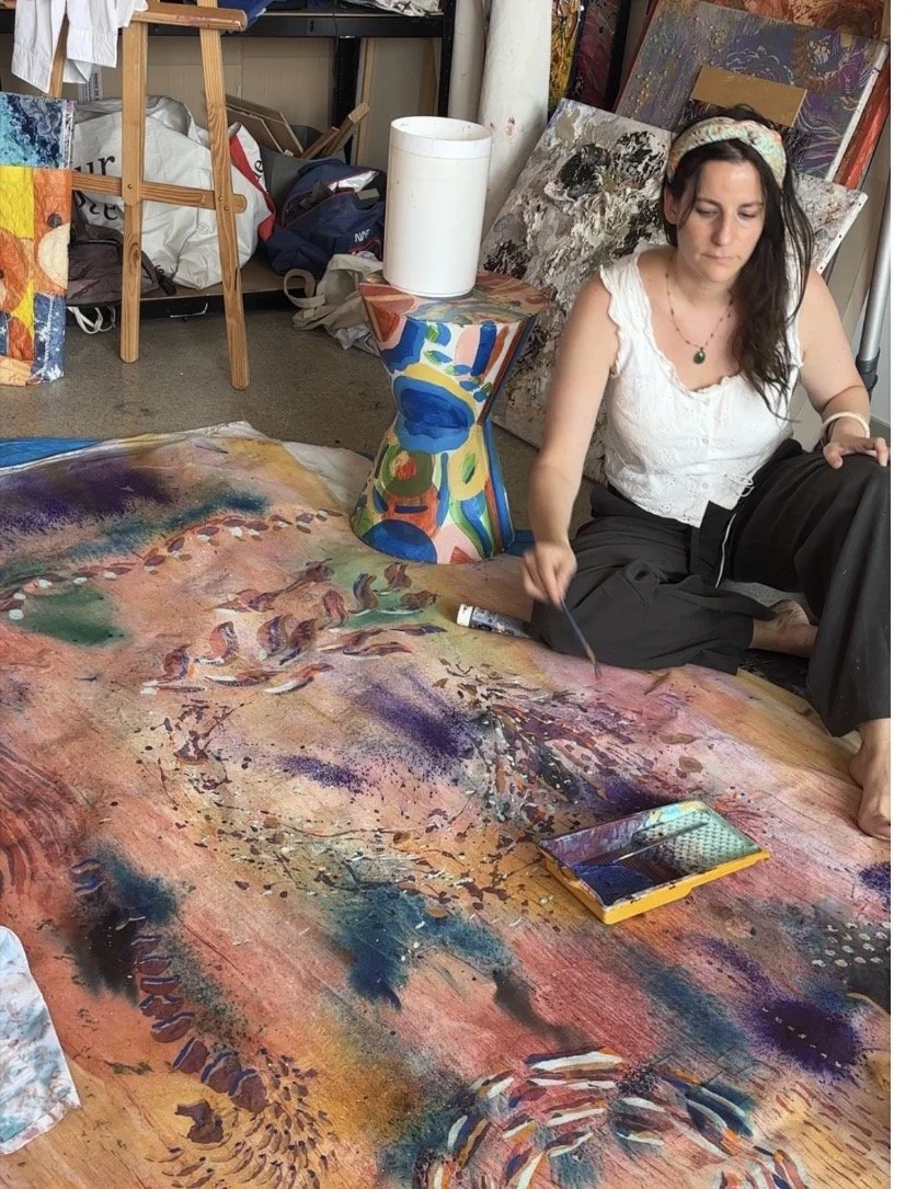 Artiste assise peignant une grande toile au sol de l'atelier