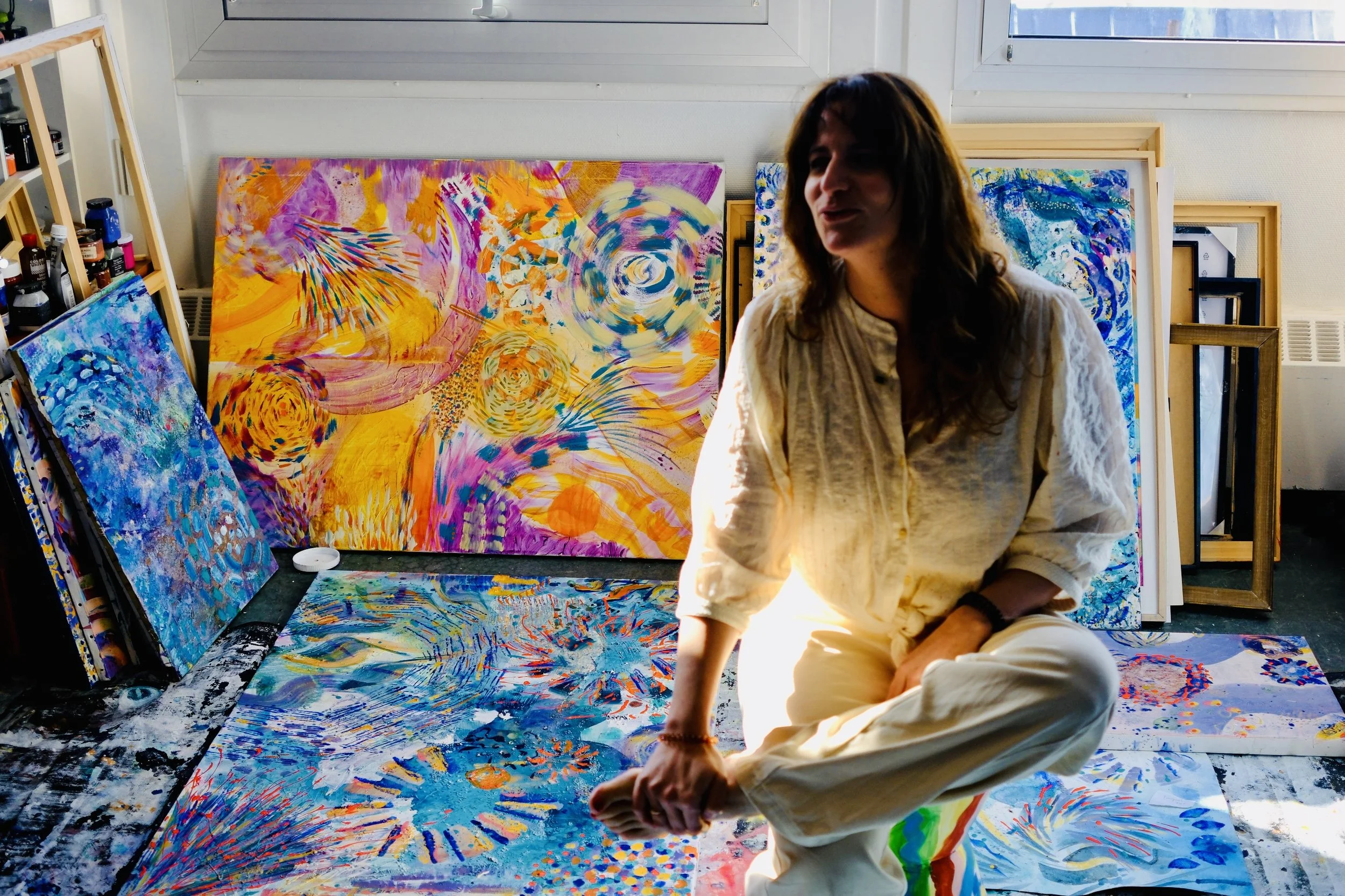 Artiste accroupie dans son atelier parmi des toiles colorées au sol