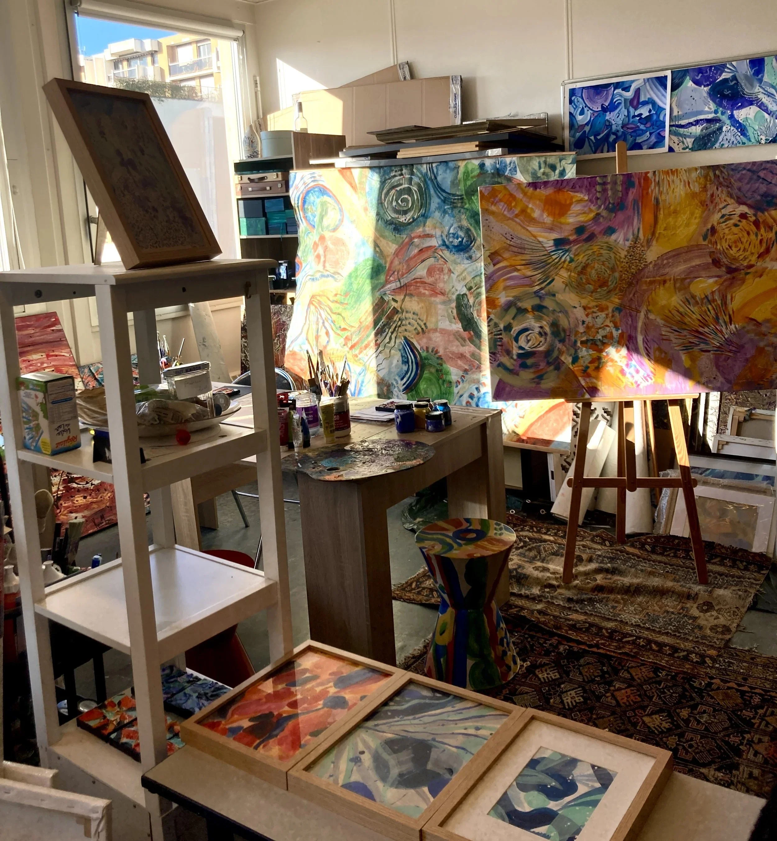 Vue d'atelier avec peintures abstraites, chevalet et cadres au sol