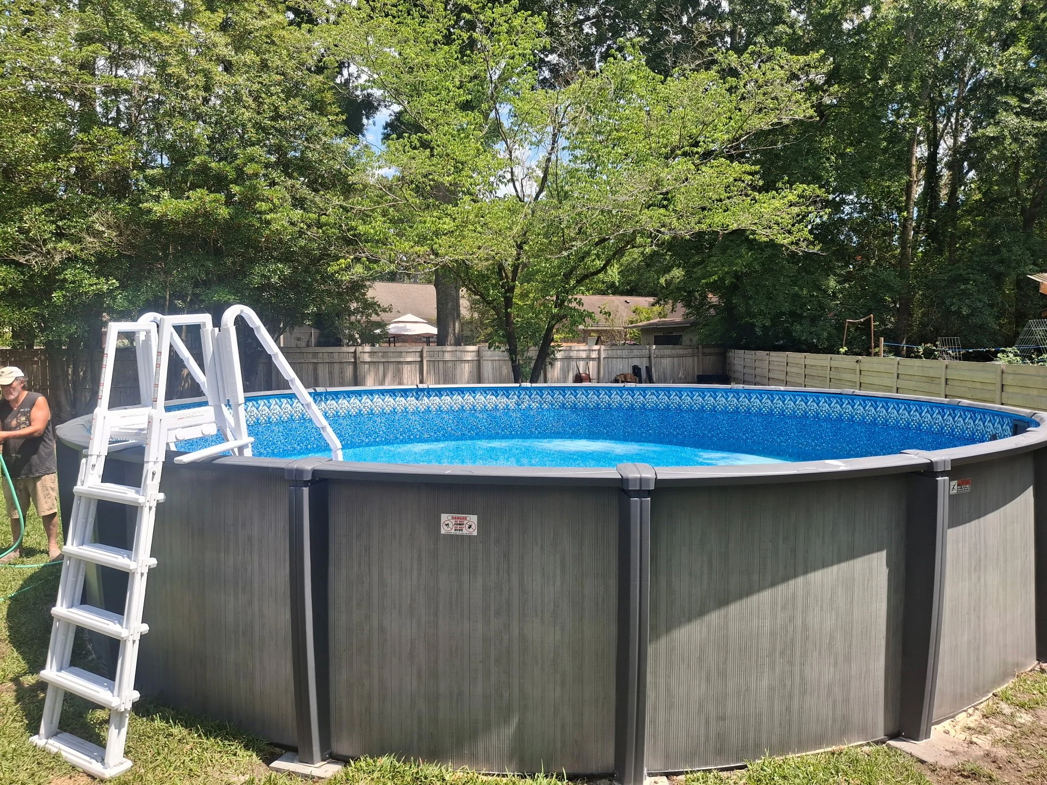 Above ground swimming pool with ladder in a fenced backyard.