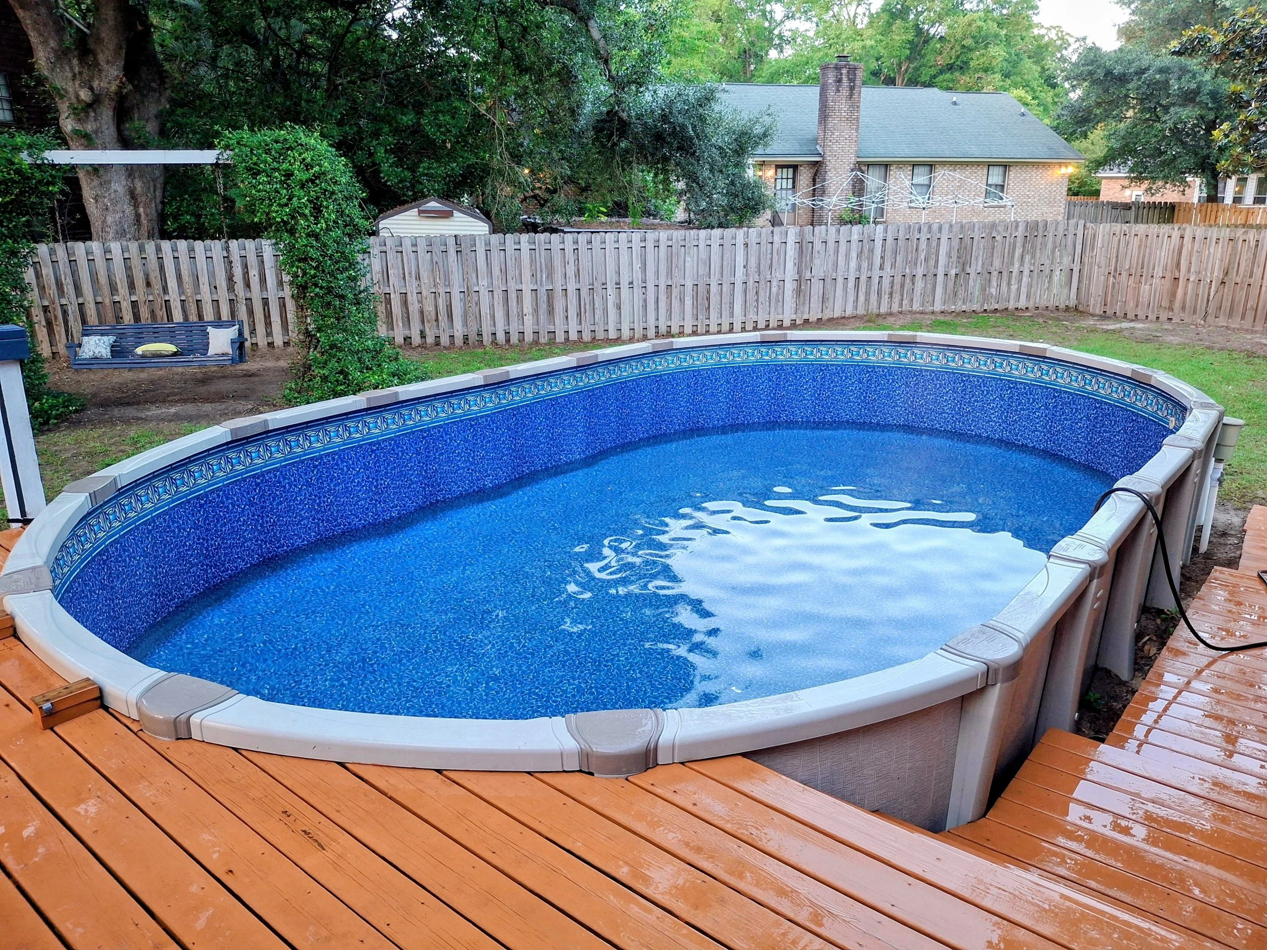Above-ground swimming pool with wood deck, backyard fence, and outdoor seating area.