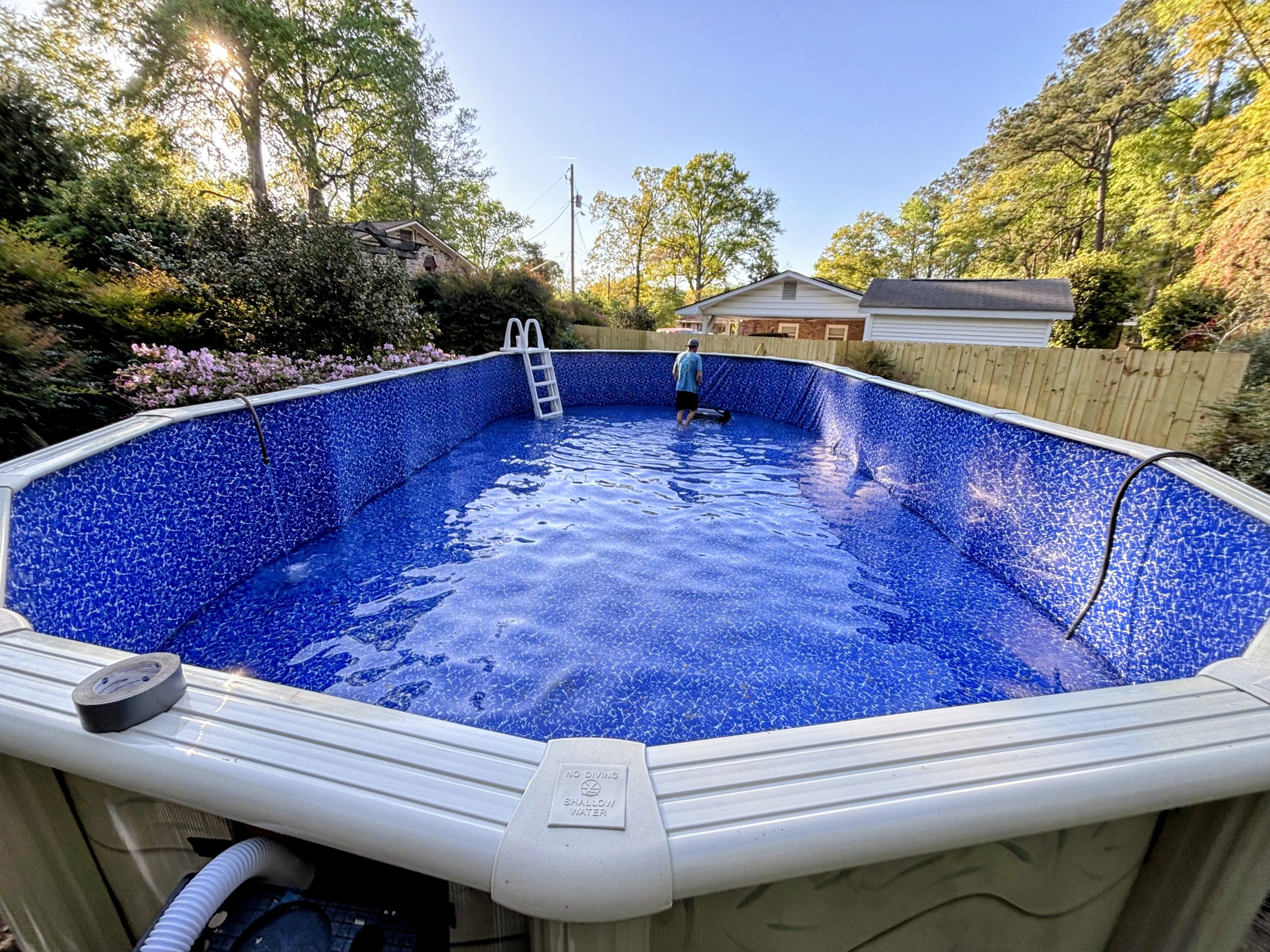 Above-ground swimming pool with white ladder in a beautiful backyard setting.