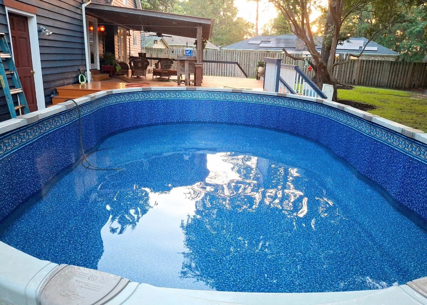Blue swimming pool with inviting water, wood deck, lawn, and outdoor furniture.