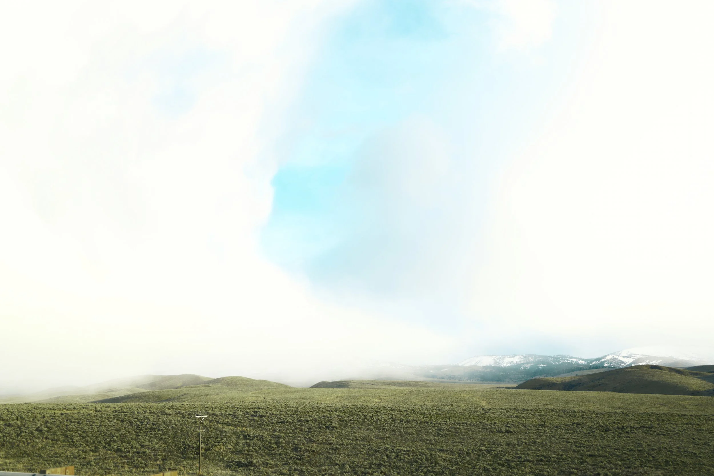 A vast landscape with green rolling hills, a snow-capped mountain in the background, and a partly cloudy sky overhead.