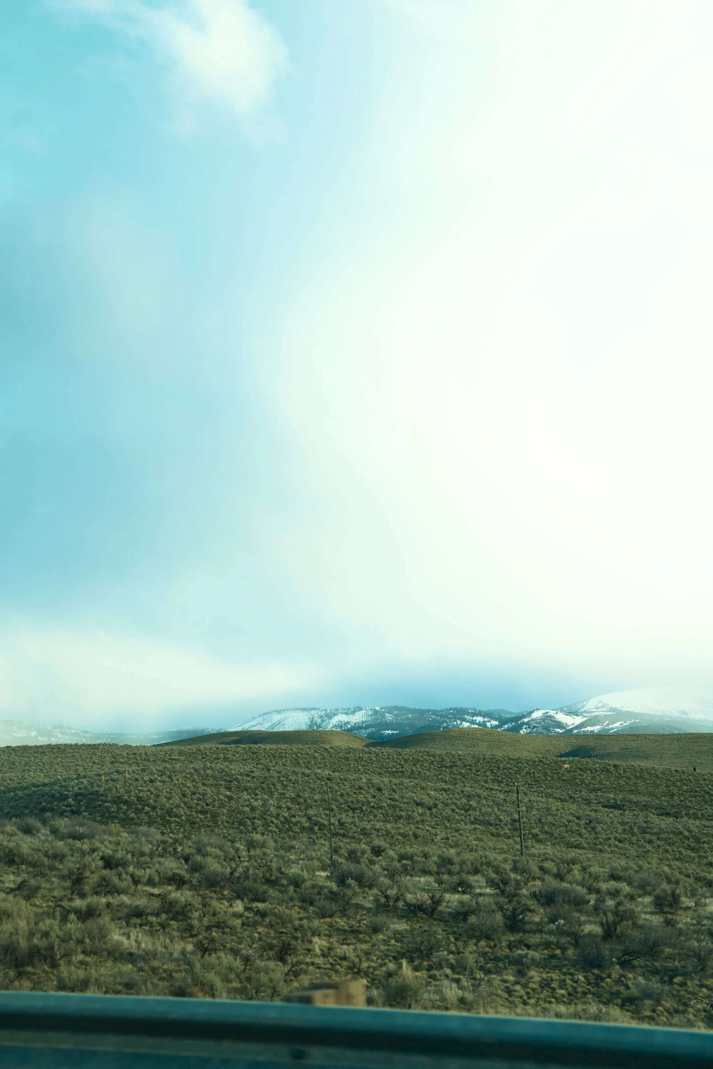 Scenic view of rolling green hills, with snow-capped mountains in the distance, under a cloudy sky.