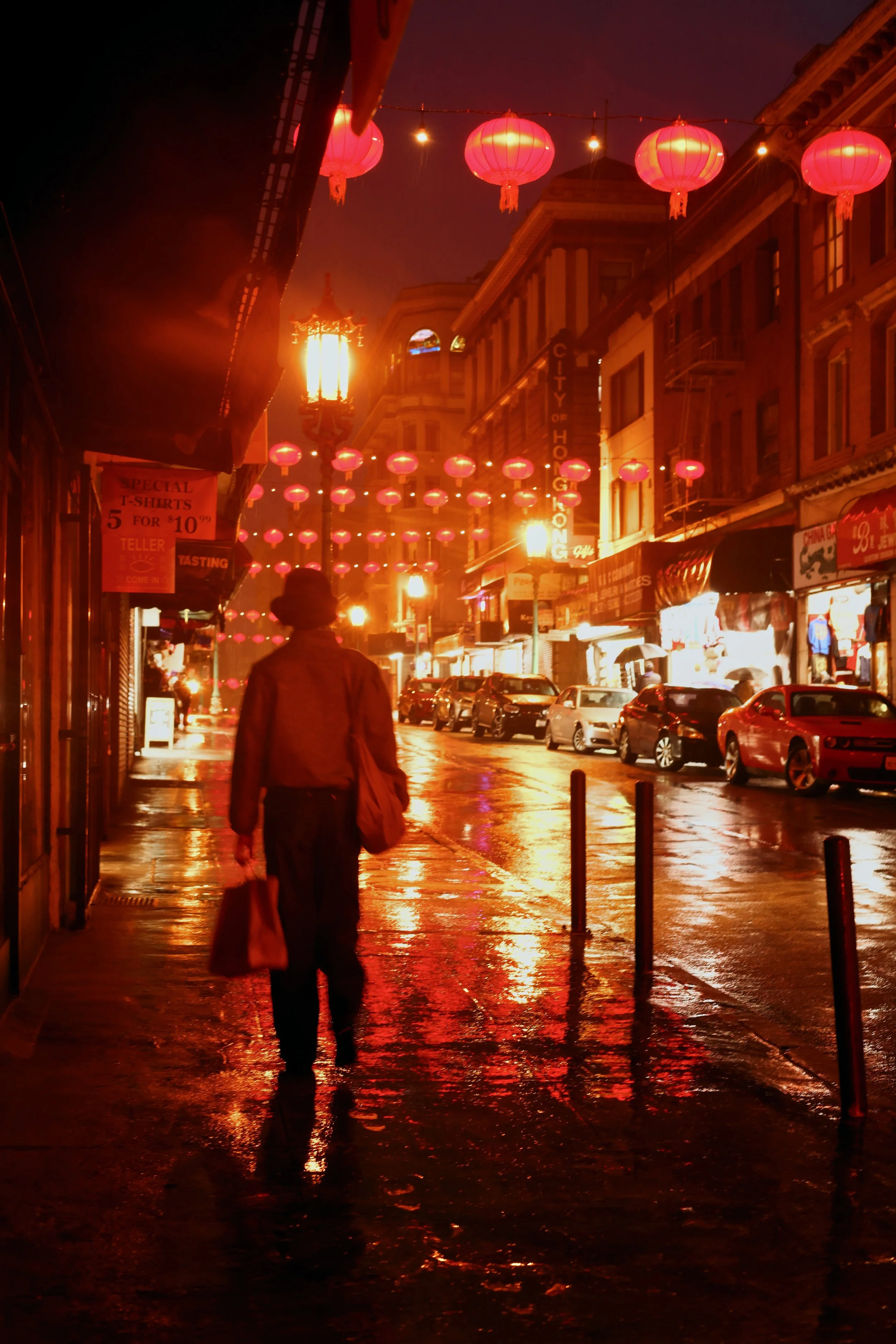 A person walking down a wet city street at night decorated with red lanterns and warm streetlights.