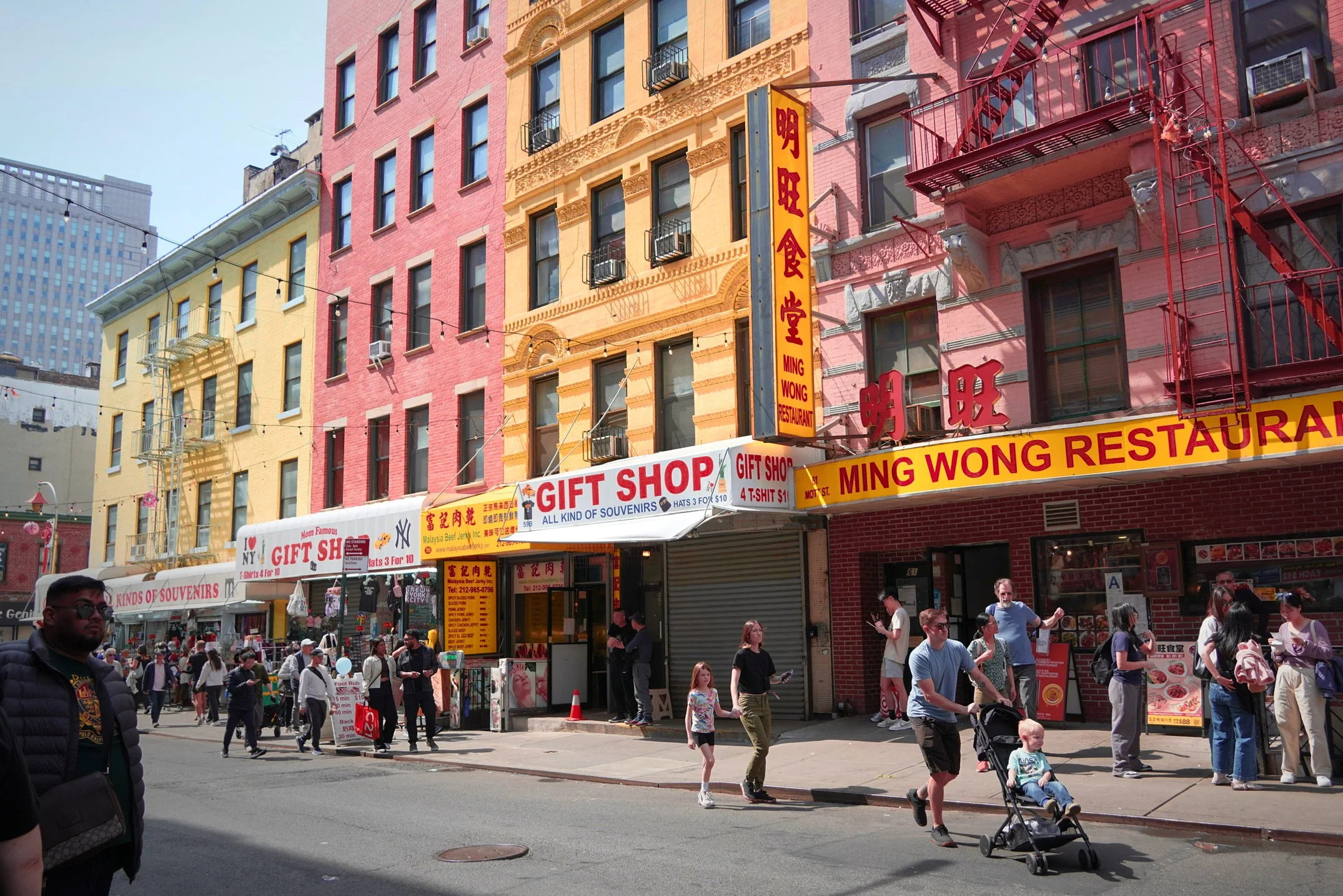 Street scene in New York City with people walking, shopping, and a colorful building with signs for a gift shop and restaurant.