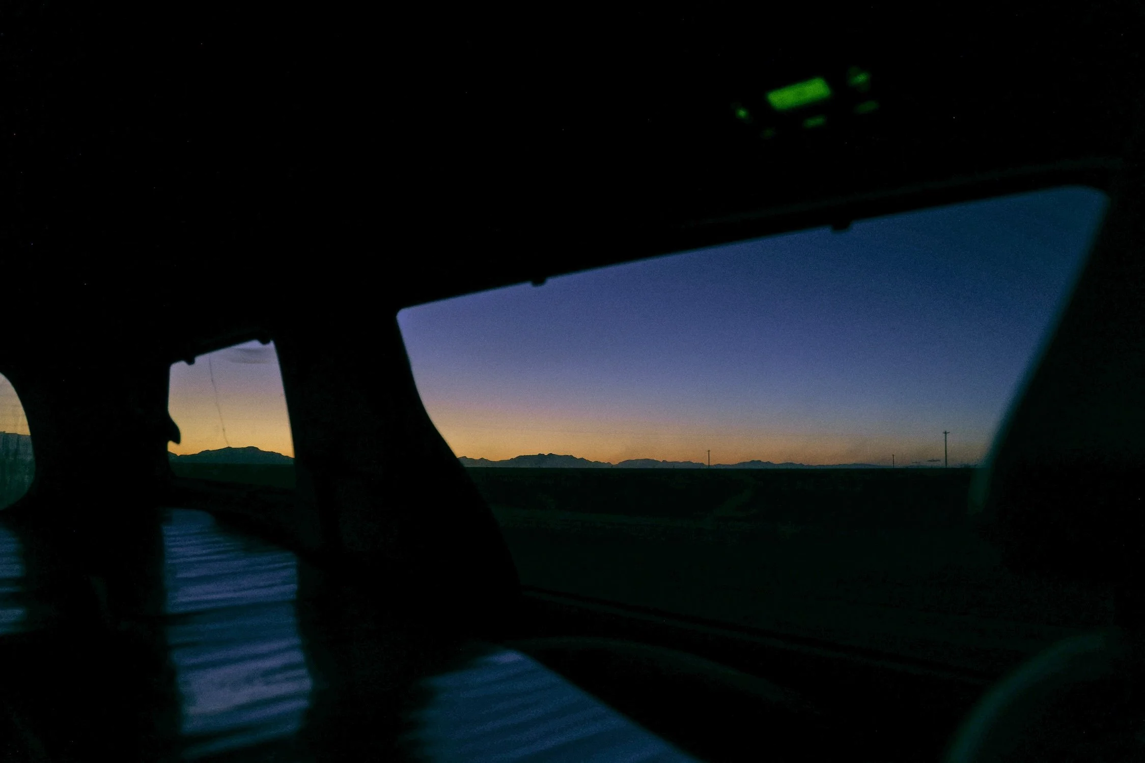 A view from inside a vehicle at dusk, showing the dashboard and windshield with mountains in the distance and a darkening sky.