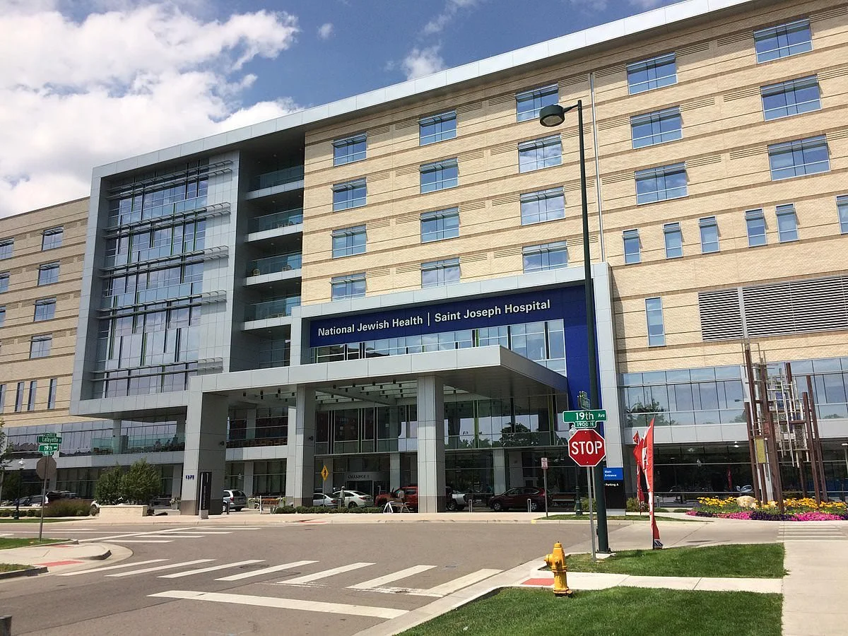 Exterior view of Saint Joseph Hospital, part of National Jewish Health, with street signs and a stop sign in front.