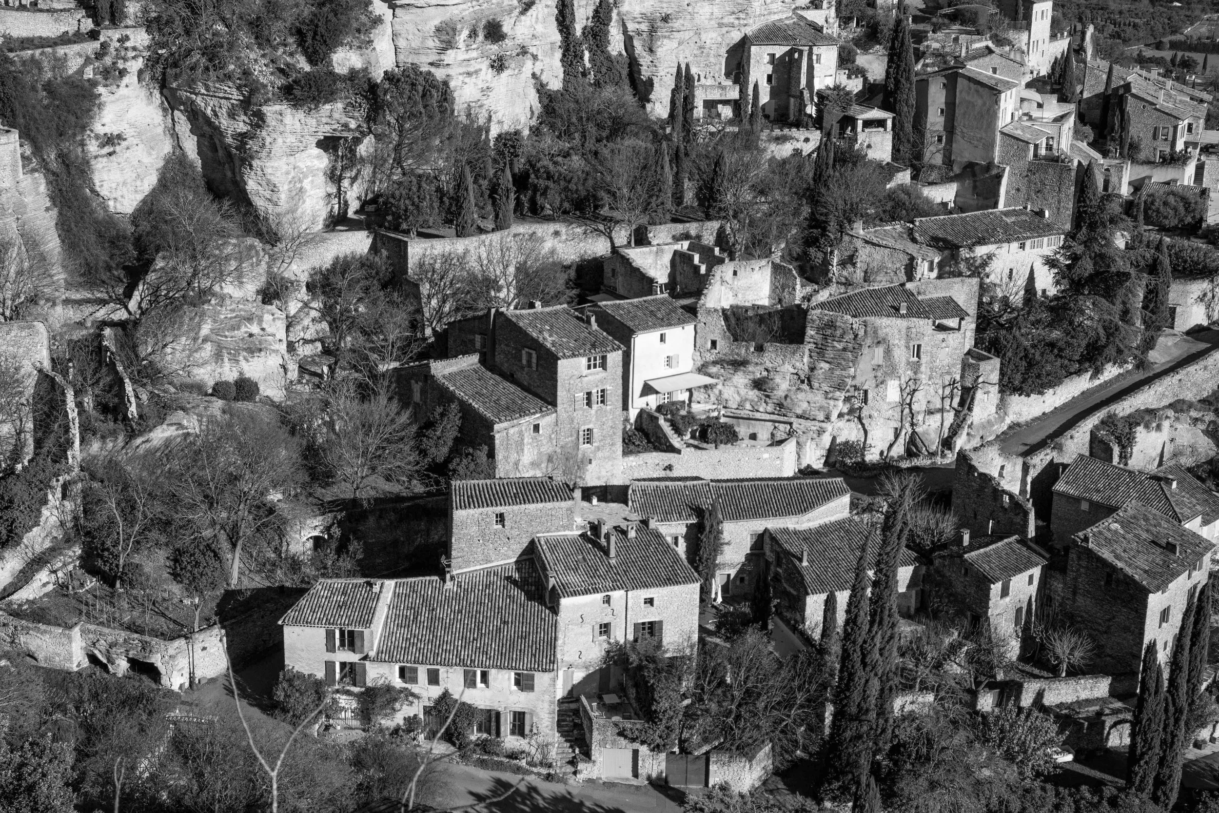 Vue aérienne d'un village patrimonial sur une colline rocheuse, avec des maisons anciennes en pierre à toit en tuiles, entouré d'un paysage protégé.