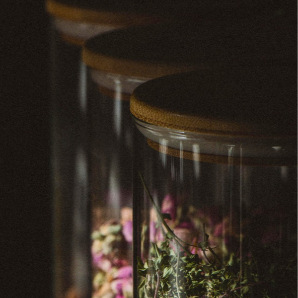 Multiple glass jars with wooden lids containing dried flowers or herbs, arranged in a row.