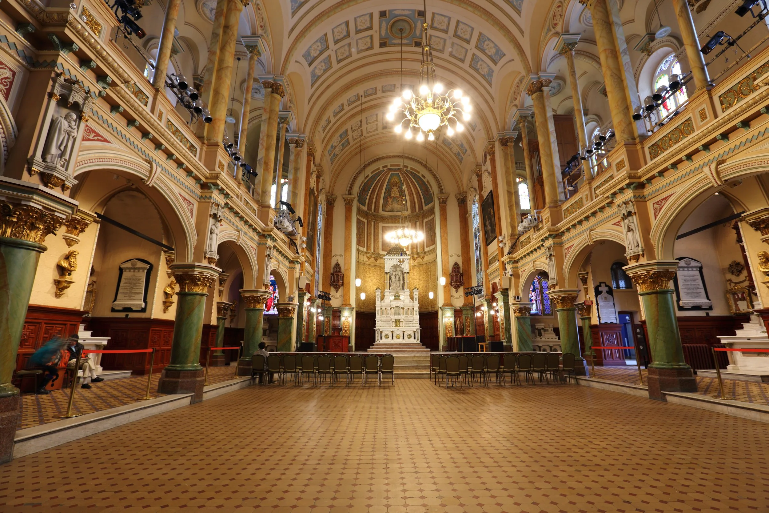 Intérieur d'une église ornée, avec un autel principal en blanc, des chandeliers suspendus, des colonnes en marbre vert et des sièges devant l'autel.