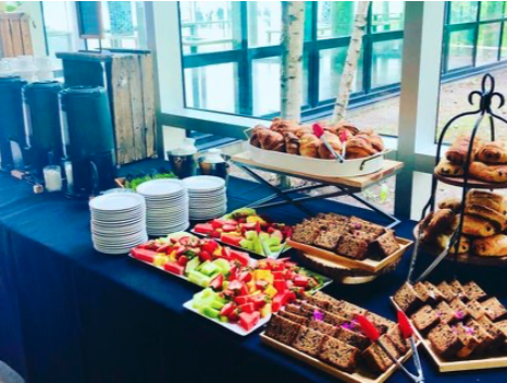 Buffet avec assiettes de fruits, gâteaux, et snacks dans une salle lumineuse.