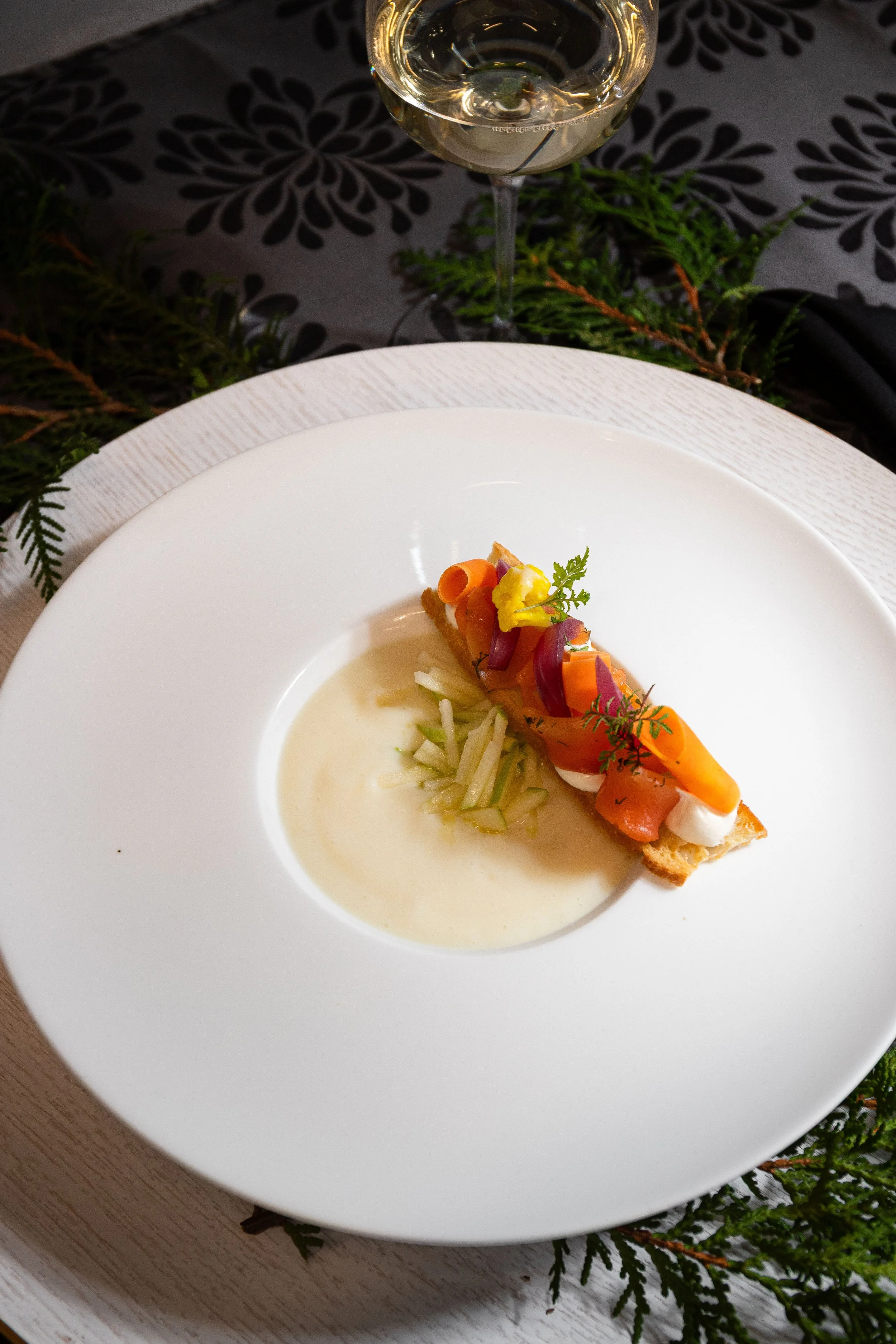 Assiette avec un plat de saumon fumé, crème, petits légumes, et herbes, accompagnée d'un verre de vin blanc.