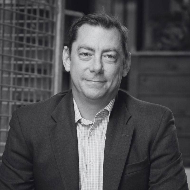 A black and white photo of a man in a suit smiling at the camera.