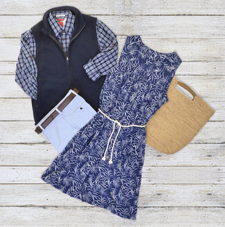 MB Sport casual outfit including a plaid shirt, navy vest, patterned blue and white dress, white belt, straw tote bag, and blue patterned earrings on a white wooden background.