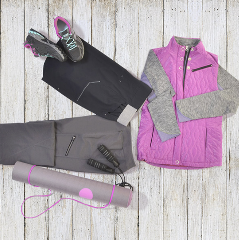 Collection of athletic clothing and gear on a wooden floor, including pink and gray jacket, black pants, athletic shoes, jump rope, and yoga mat.
