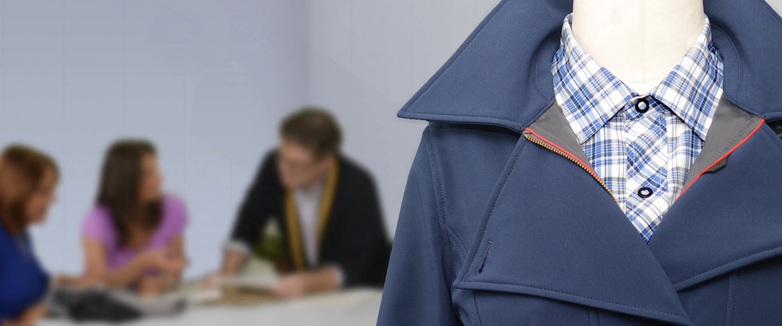 Close-up of a MB Sport mannequin dressed in a blue jacket and plaid shirt with three people blurred in the background, likely in a meeting or discussion.