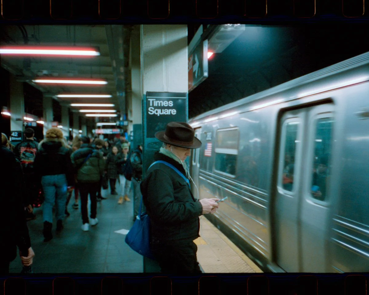 People waiting on the subway platform at Times Square station, with a moving train next to them.