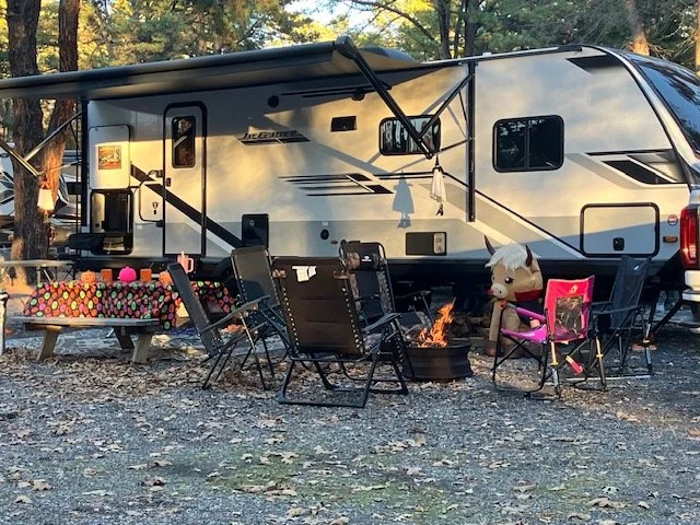 An RV Site with lawn chairs and picnic table and a fire pit