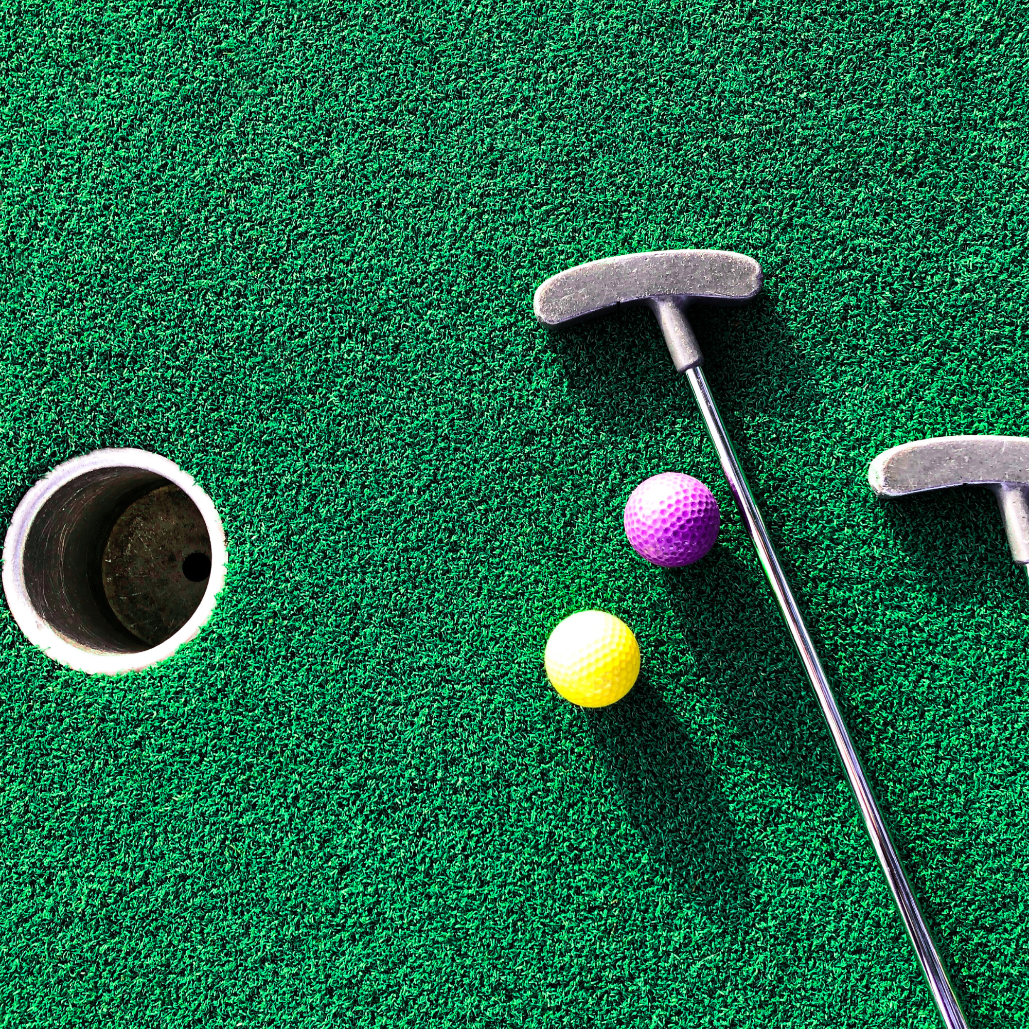 Photo of a mini golf hole with a putter and golf balls nearby.