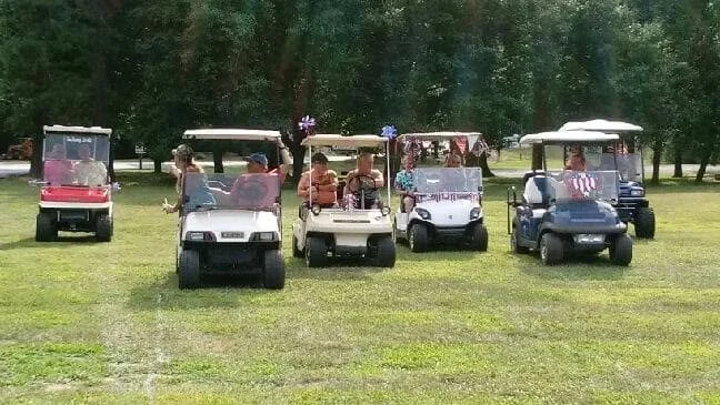A group of 4 golf carts on a open field with trees in the background.